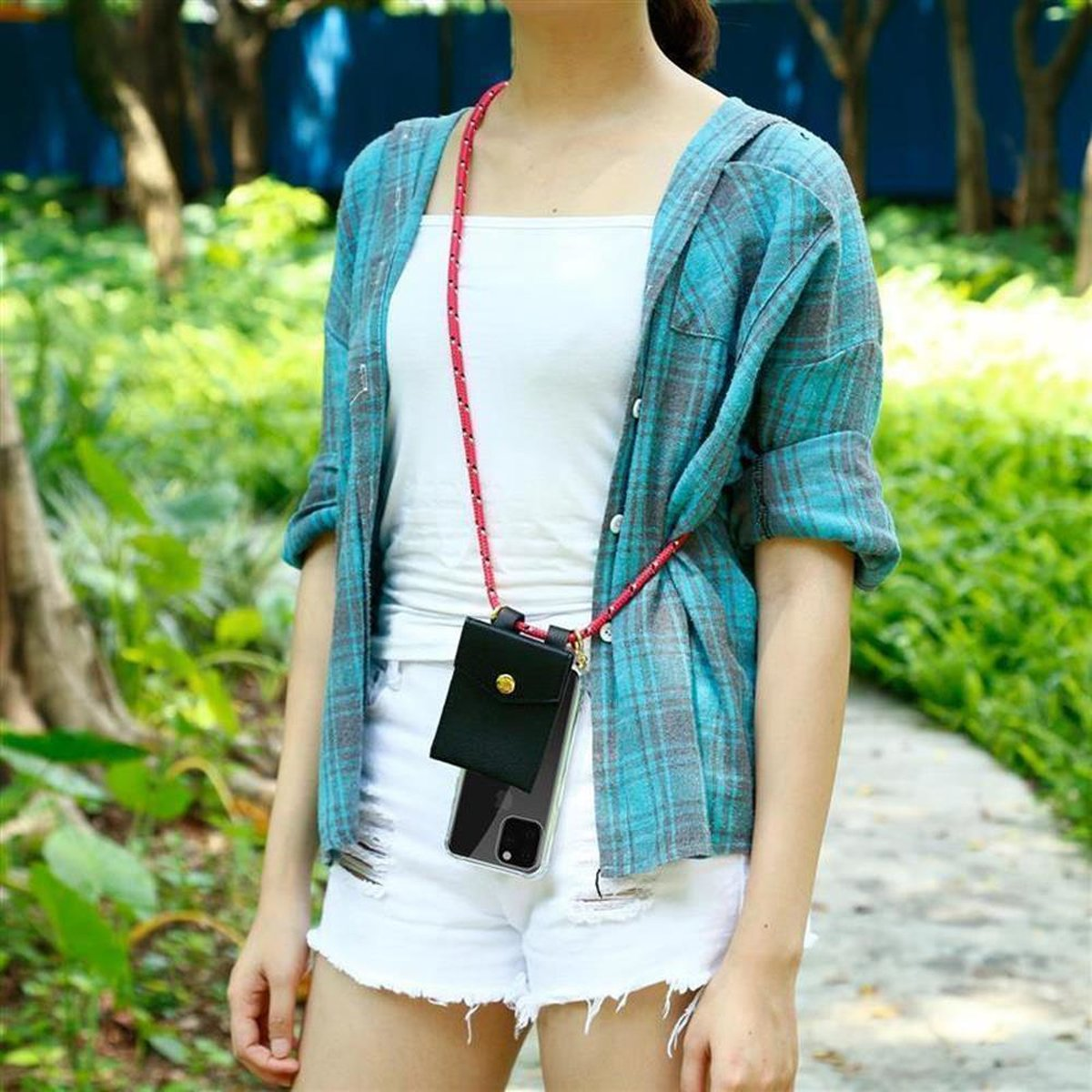 Una donna che indossa una camicia a quadri e pantaloncini bianchi ha un telefono in una custodia intorno al collo.
