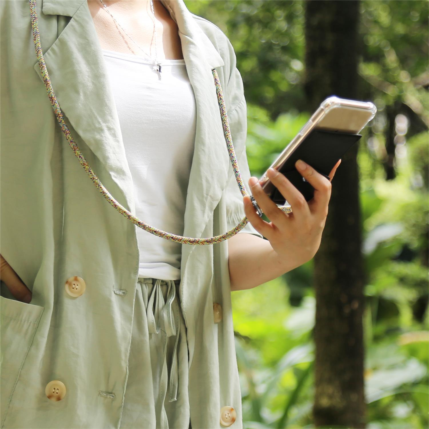 Donna che tiene un telefono con un cordino. Indossa un cappotto verde chiaro, una camicia e pantaloni bianchi.