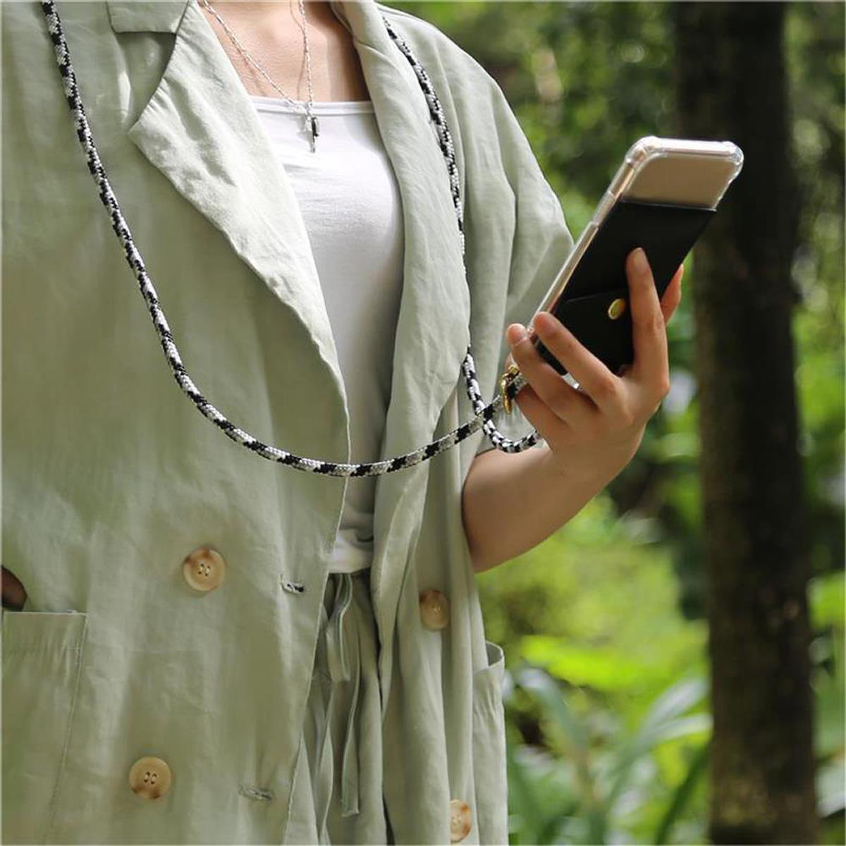Donna che tiene in mano un telefono in una custodia nera con un cordino bianco e nero. Indossa una giacca verde. Sfondo verde.