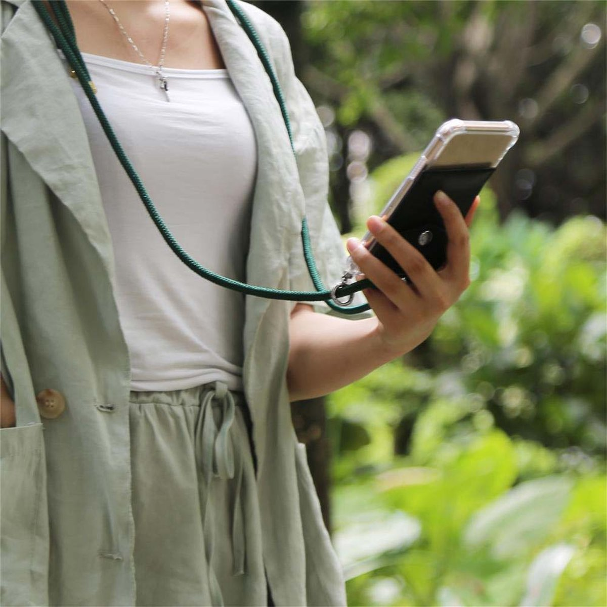 Una persona in abiti verde chiaro tiene in mano un telefono con un cordino verde. Fogliame verde sullo sfondo.