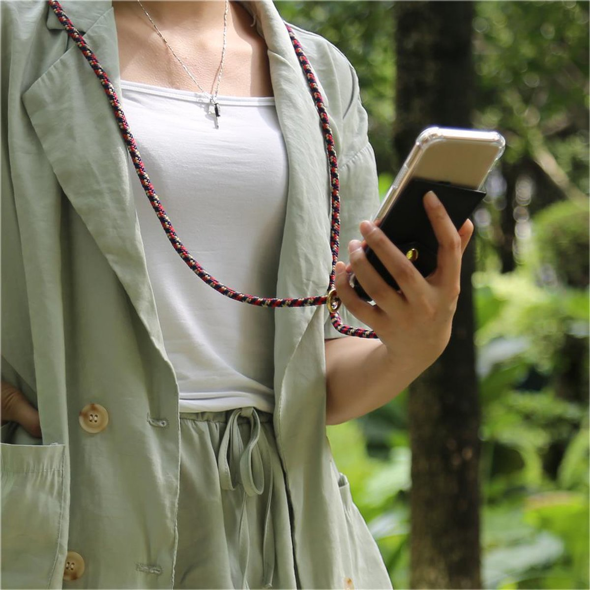 Una persona che tiene un telefono con un cinturino. Indossa una giacca verde e una camicia bianca. Lo sfondo è verde.