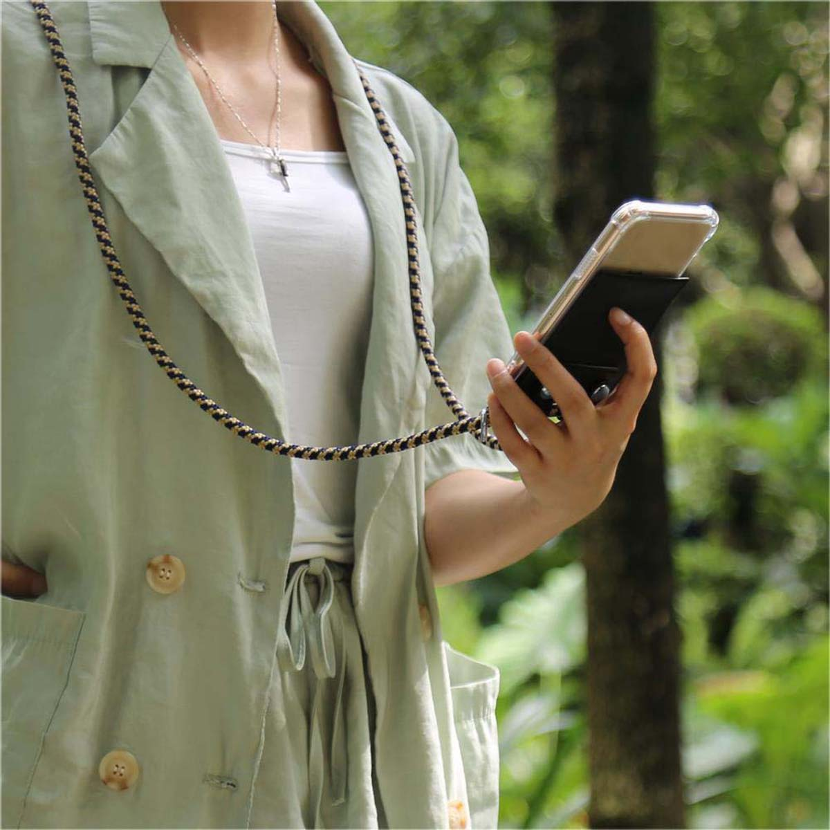 Donna che tiene un telefono in una custodia trasparente con un cordino. Indossa una camicia verde.