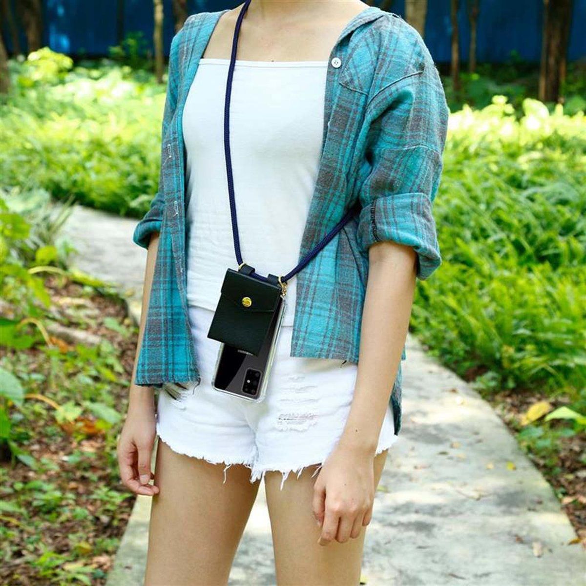 Donna con top bianco, camicia blu e pantaloncini bianchi con custodia per telefono. Alberi verdi sullo sfondo.