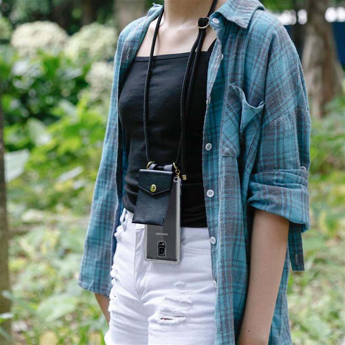 Donna con custodia nera per telefono al collo, camicia a quadri blu, pantaloncini bianchi e top nero.