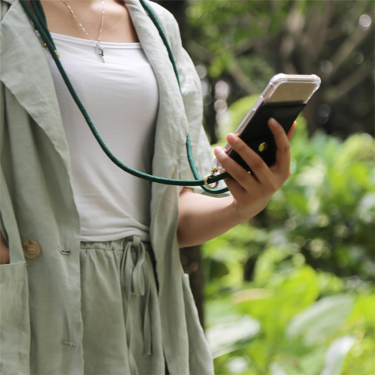 Persona che tiene un telefono con custodia a cordino. La scena è all'aperto in un ambiente verde.