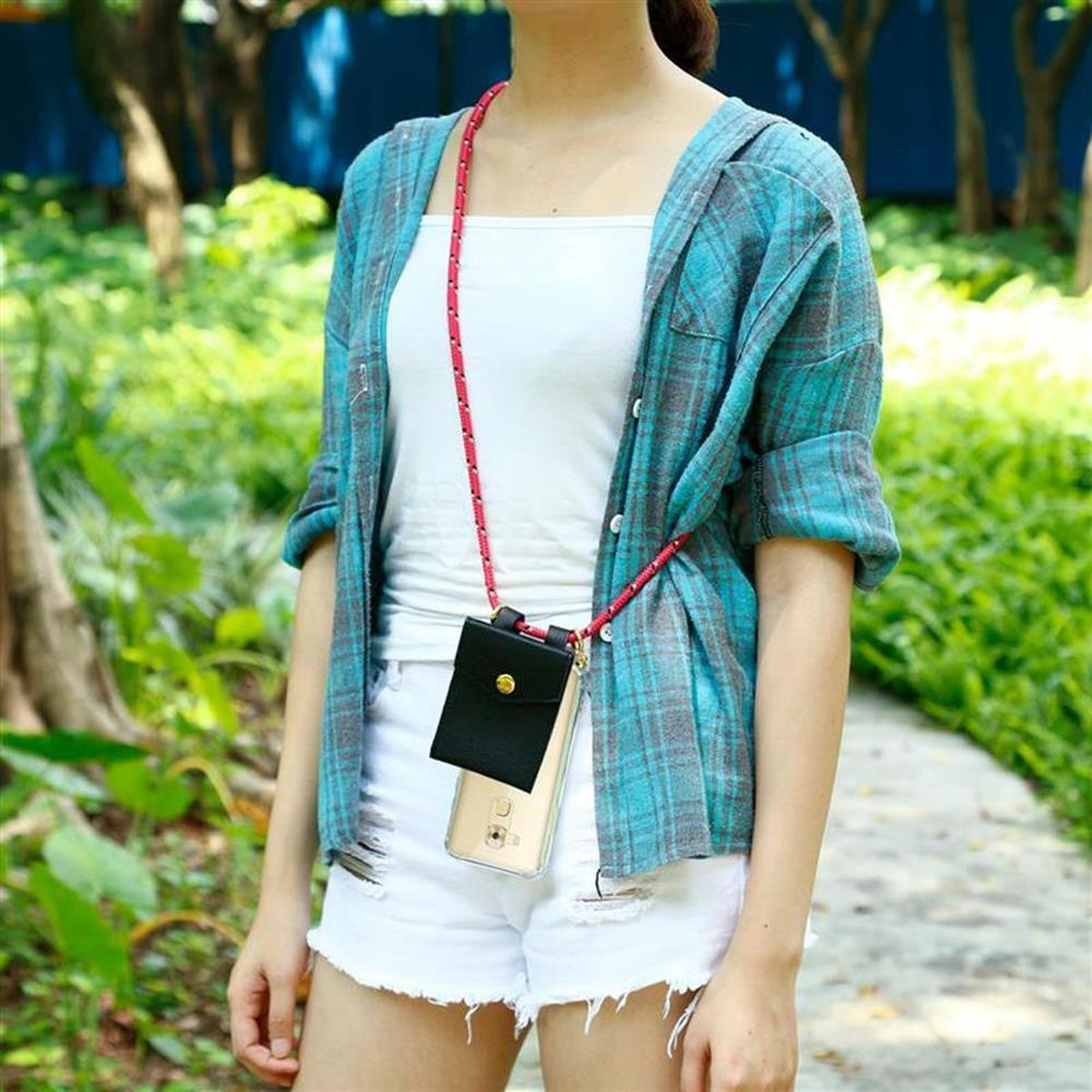 Una donna con top bianco, pantaloncini e camicia a quadri blu. Una custodia per telefono è appesa al collo.
