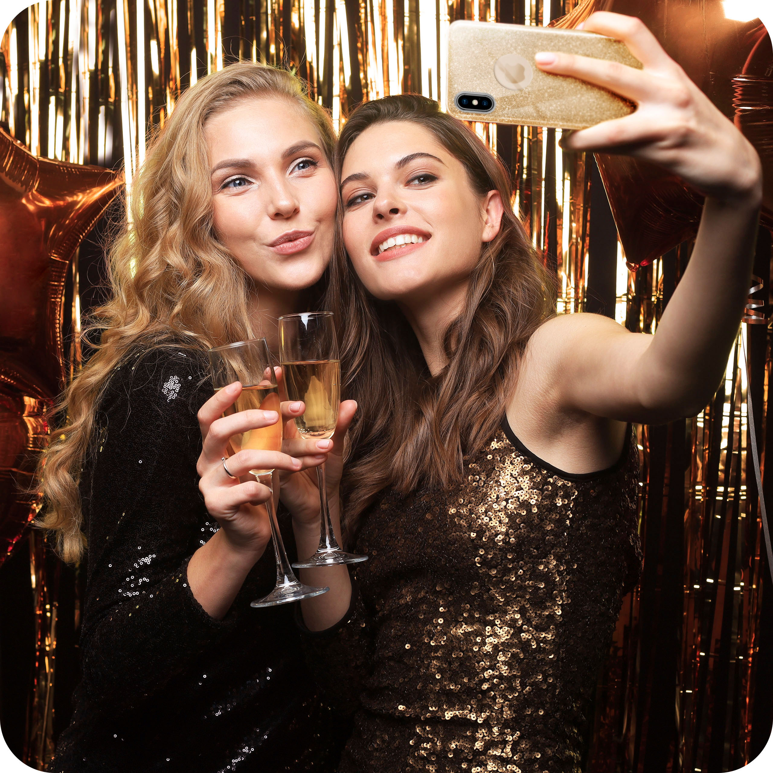Zwei Frauen machen ein Selfie mit einem goldenen Telefon; sie halten jeweils ein Sektglas, goldener Hintergrund.