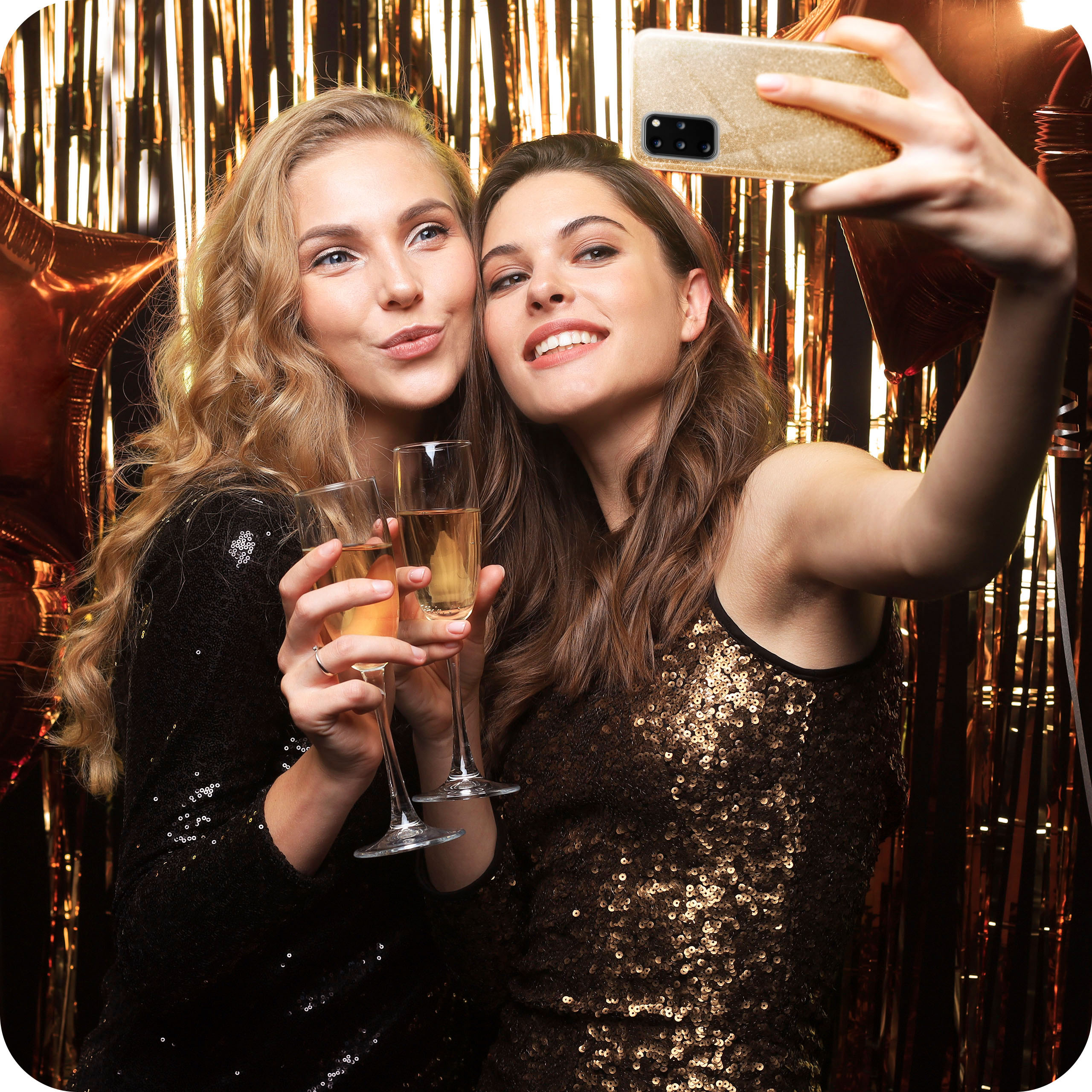 Zwei Frauen machen ein Selfie mit Champagnergläsern vor goldenen Luftschlangen.