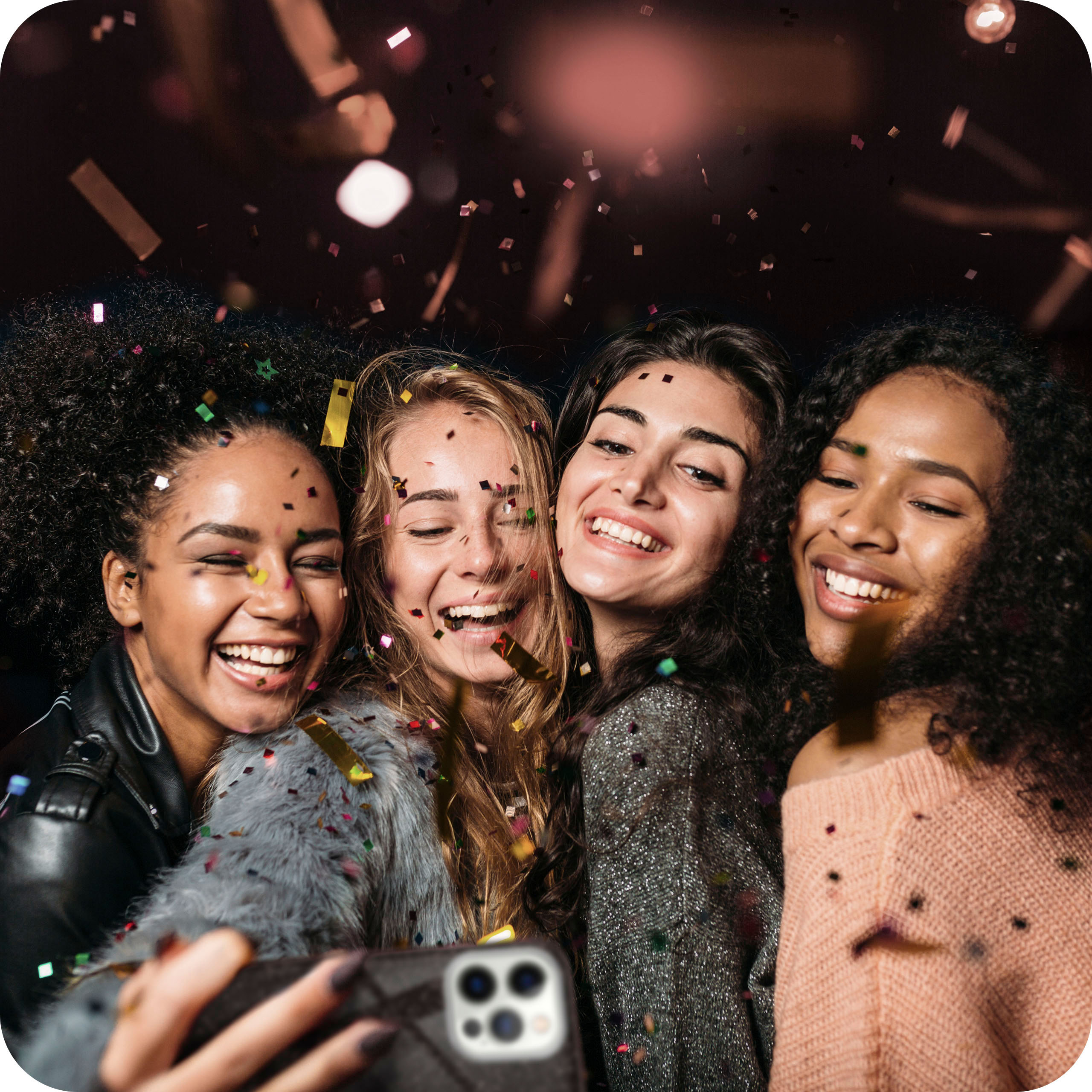 Vier Frauen machen ein Selfie, lächelnd. Konfetti fällt um sie herum.
