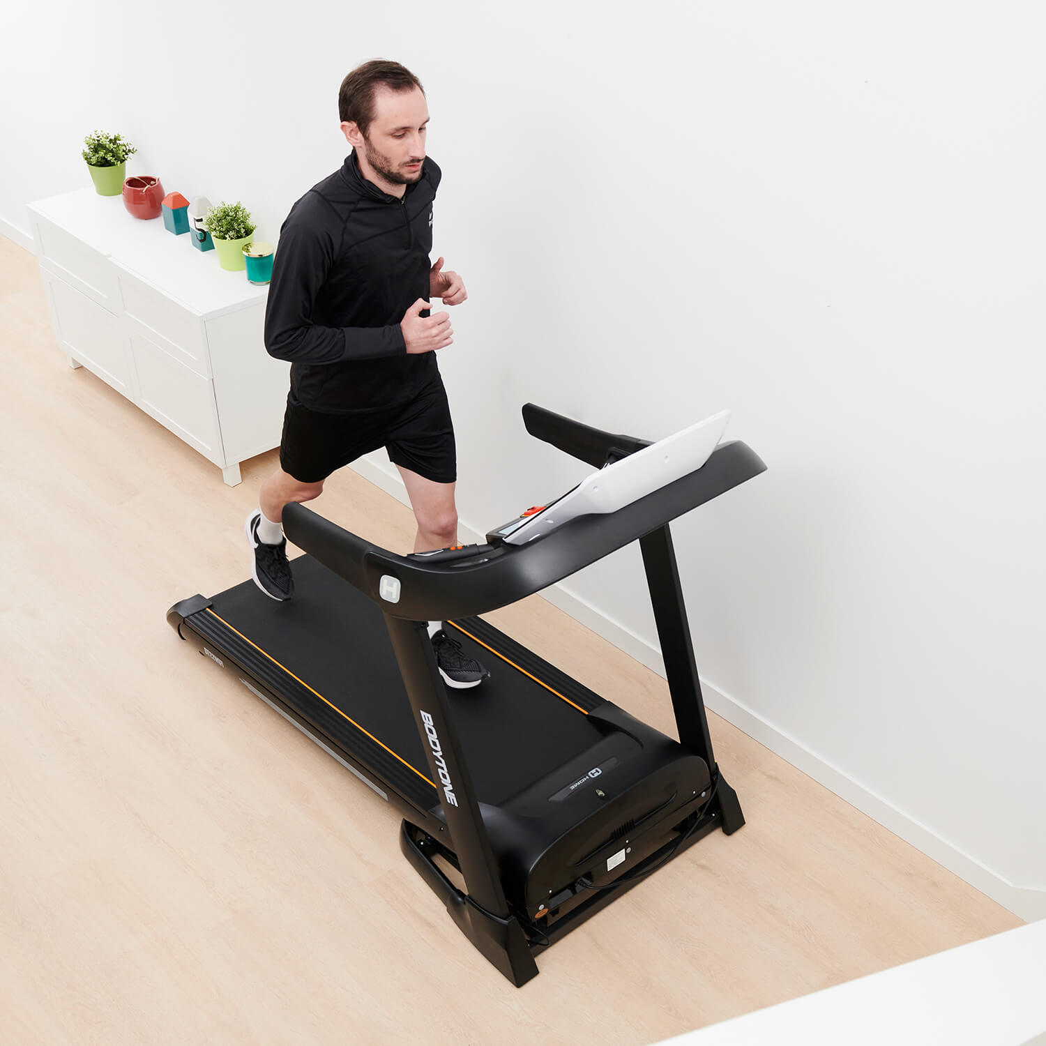 Un uomo corre su un tapis roulant in una stanza con pareti bianche.