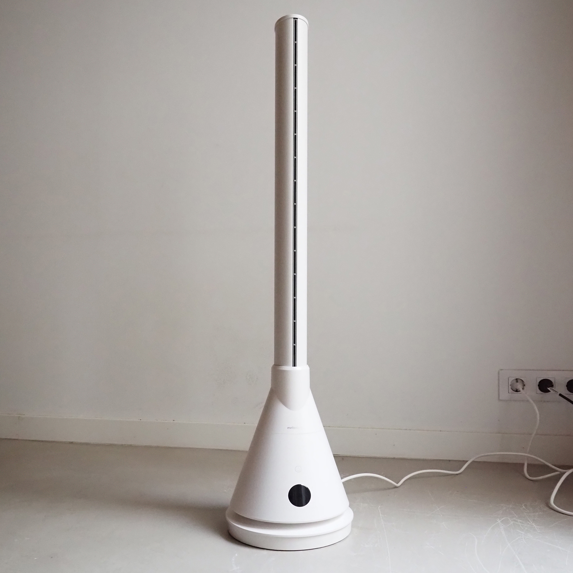 Ventilador de torre blanco en suelo gris claro, contra pared blanca, enchufes.