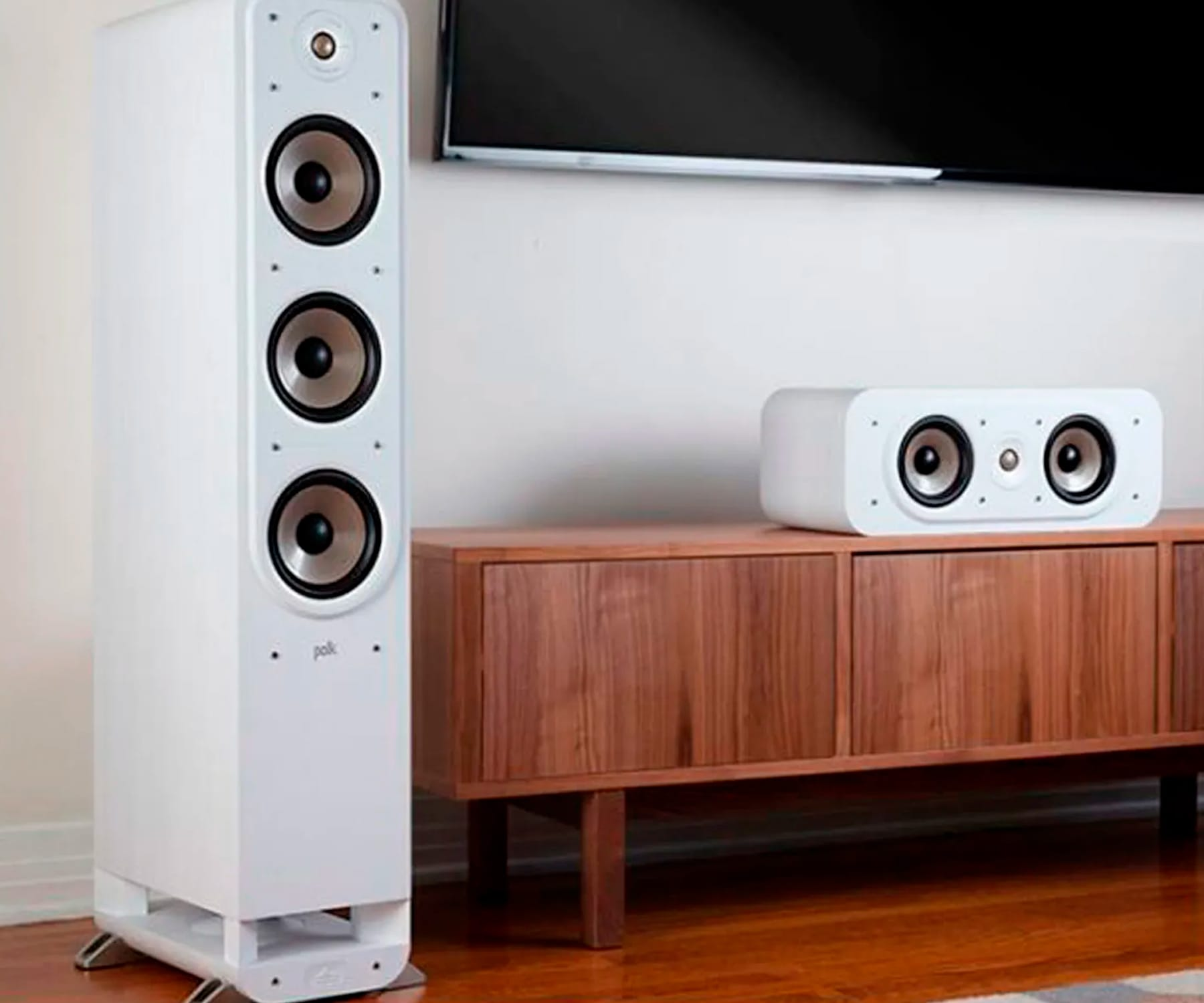 Altavoces blancos y un mueble de madera con un televisor encima. Los altavoces tienen tres altavoces negros.