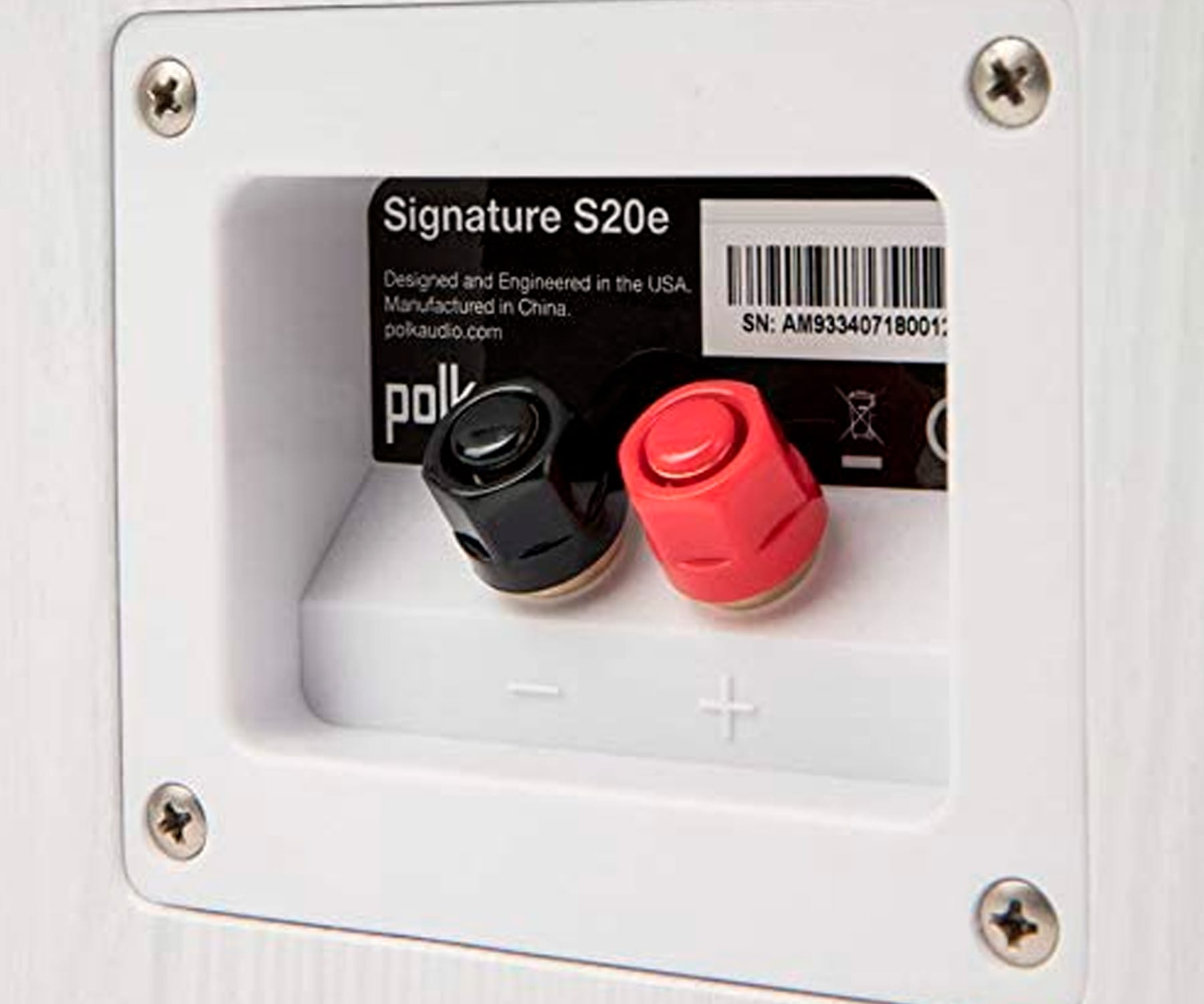Primer plano de terminales de altavoz. Conectores negros y rojos en un panel blanco empotrado.