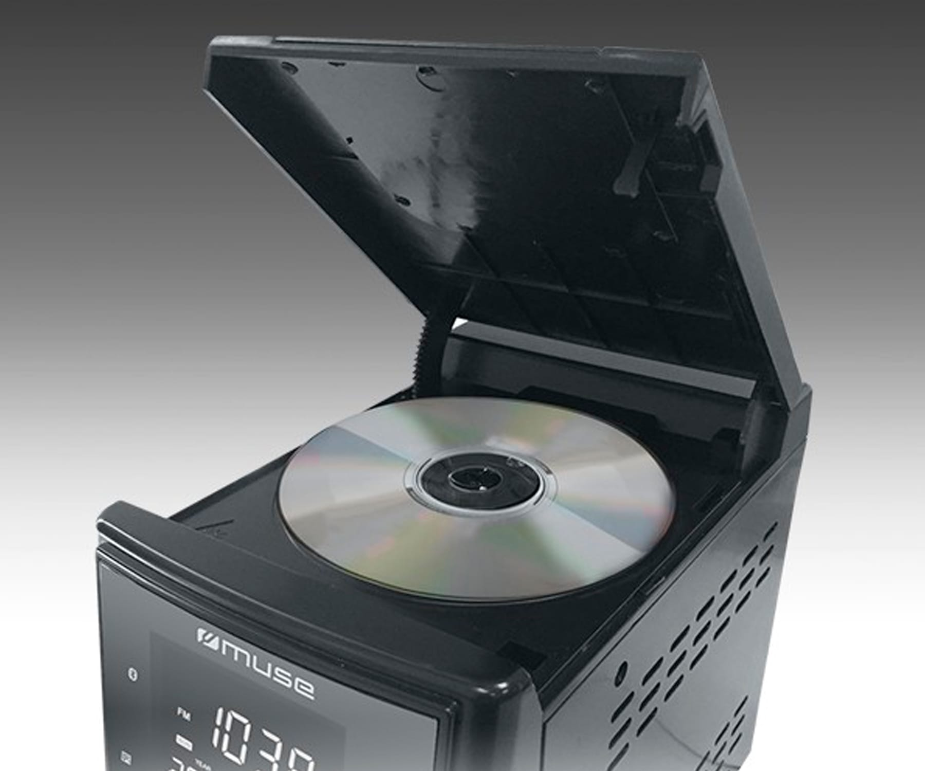 Reproductor de CD negro mostrando "Muse" y hora. Un CD está dentro, tapa abierta, sobre fondo gris.