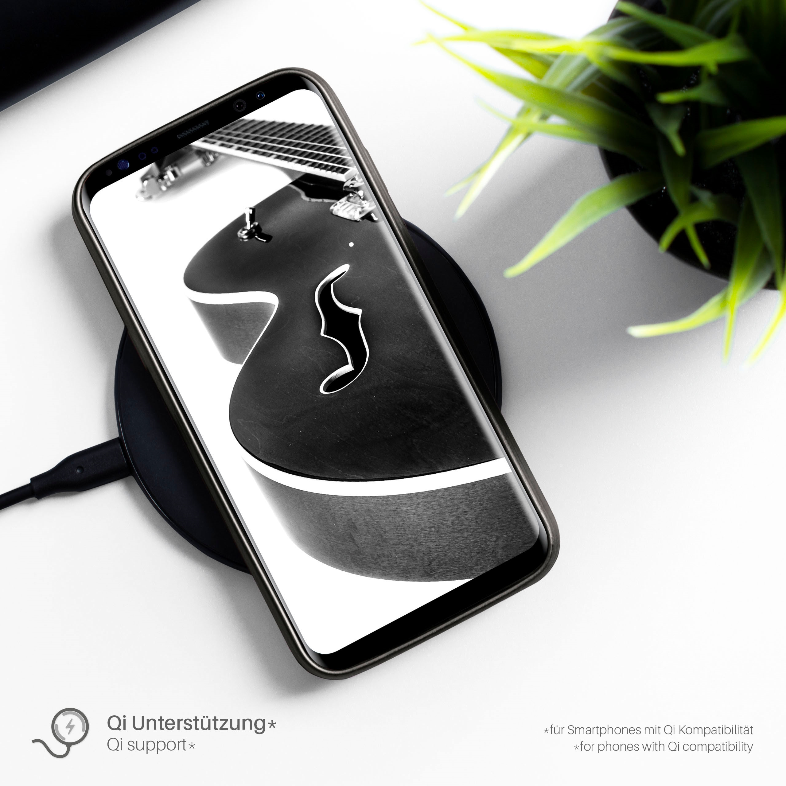 Telefon auf kabellosem Ladegerät, schwarze Hülle, Gitarrenbild auf dem Bildschirm. Deutsch.