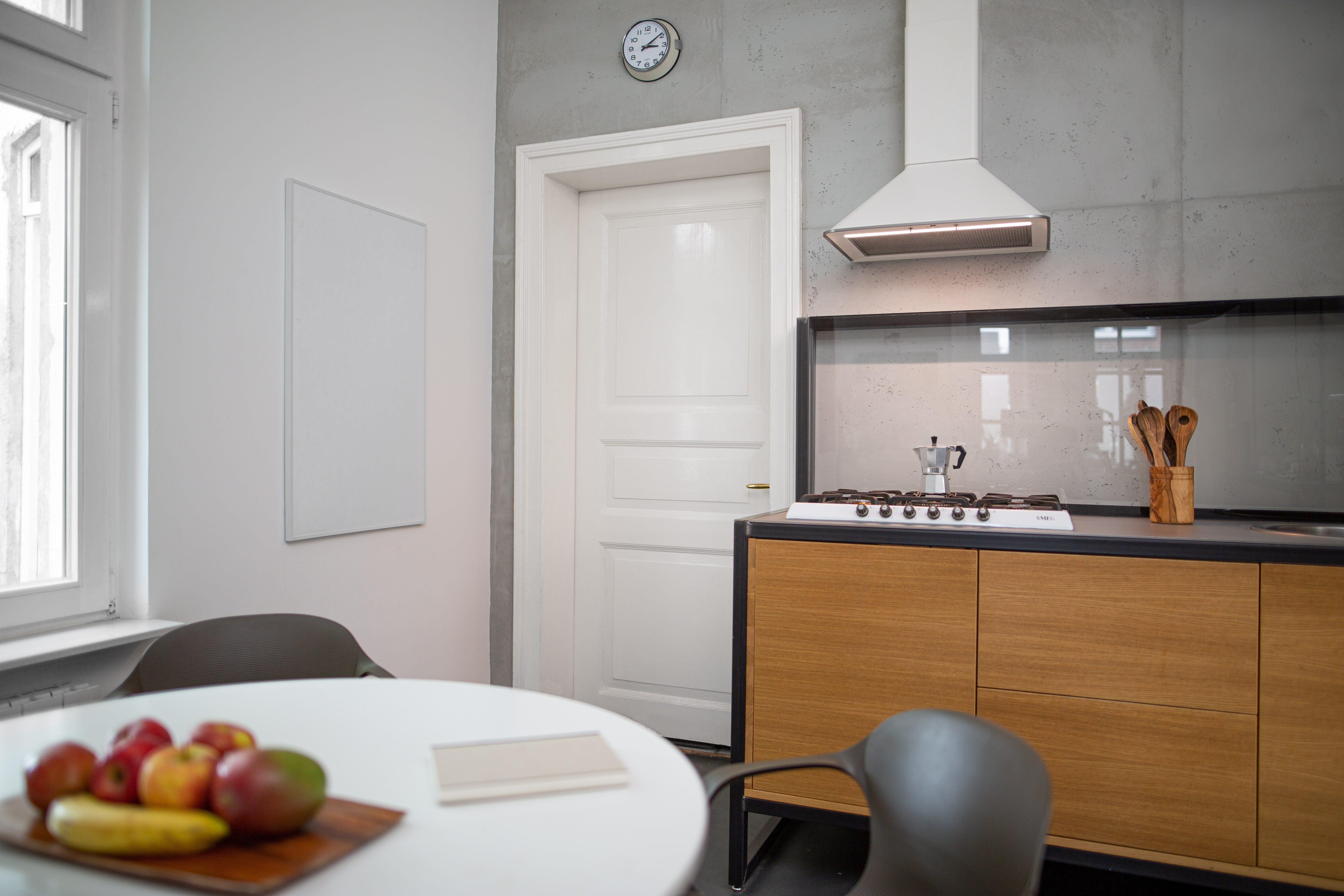 Eine Kücheneinrichtung. Ein Tisch mit Essen, ein Herd mit Topf und eine Uhr an der Wand.