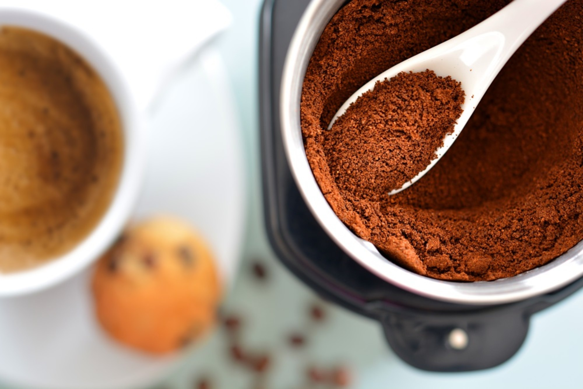 Filiżanka kawy z kawą i łyżką w pojemniku z fusami. Małe ciastko jest obok.
