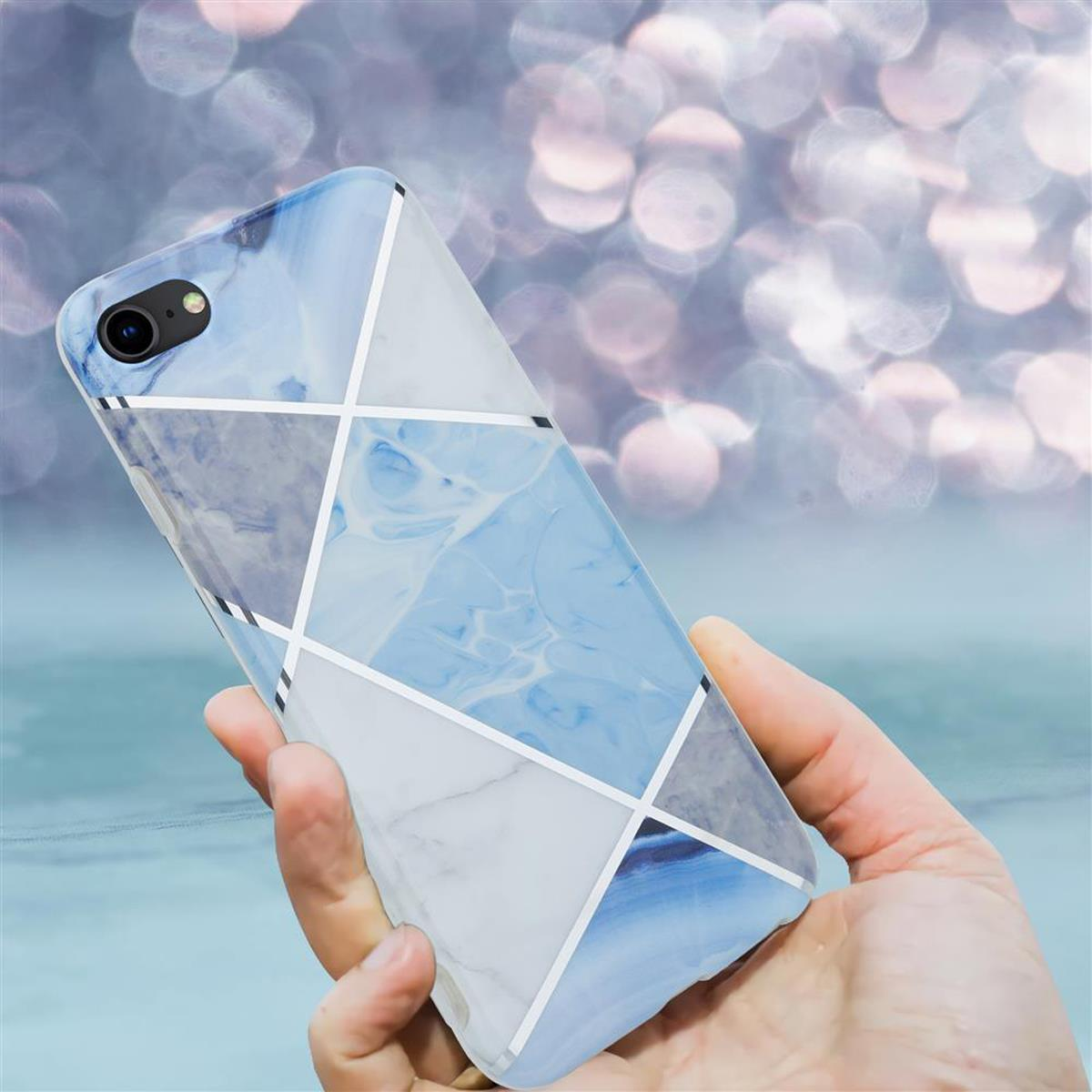 Una mano che tiene una custodia per telefono con un motivo simile al marmo con colori blu, grigio e bianco, su uno sfondo sfocato.