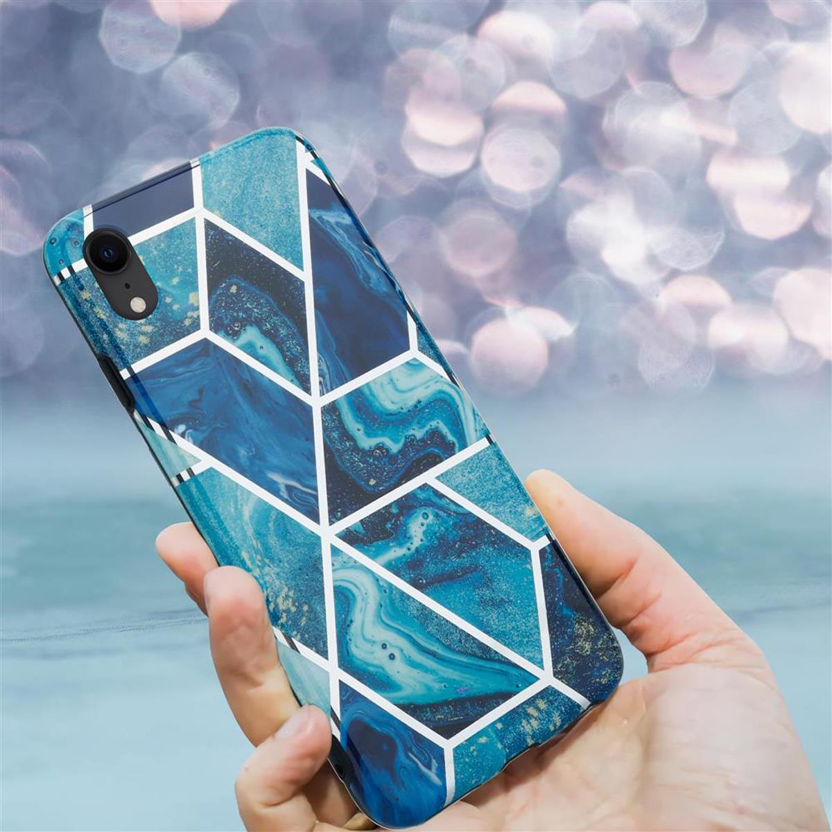 Una mano che tiene uno smartphone con una custodia blu a motivo marmorizzato. La custodia ha linee geometriche bianche.