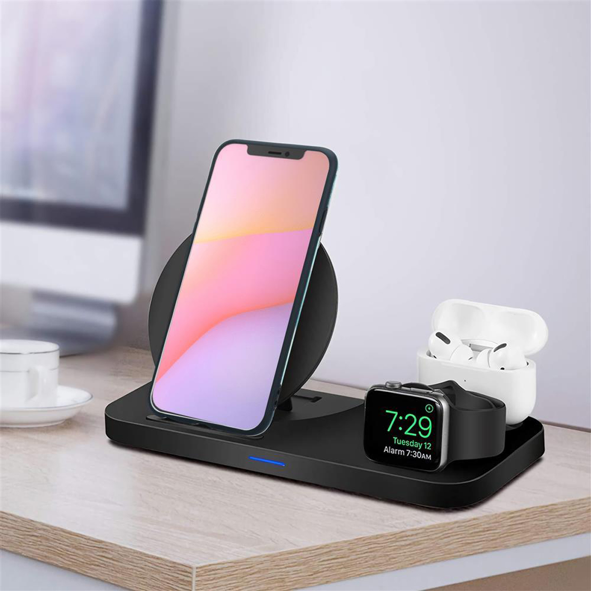 Stazione di ricarica wireless con telefono, orologio e auricolari. Scrivania in legno e sfondo sfocato.