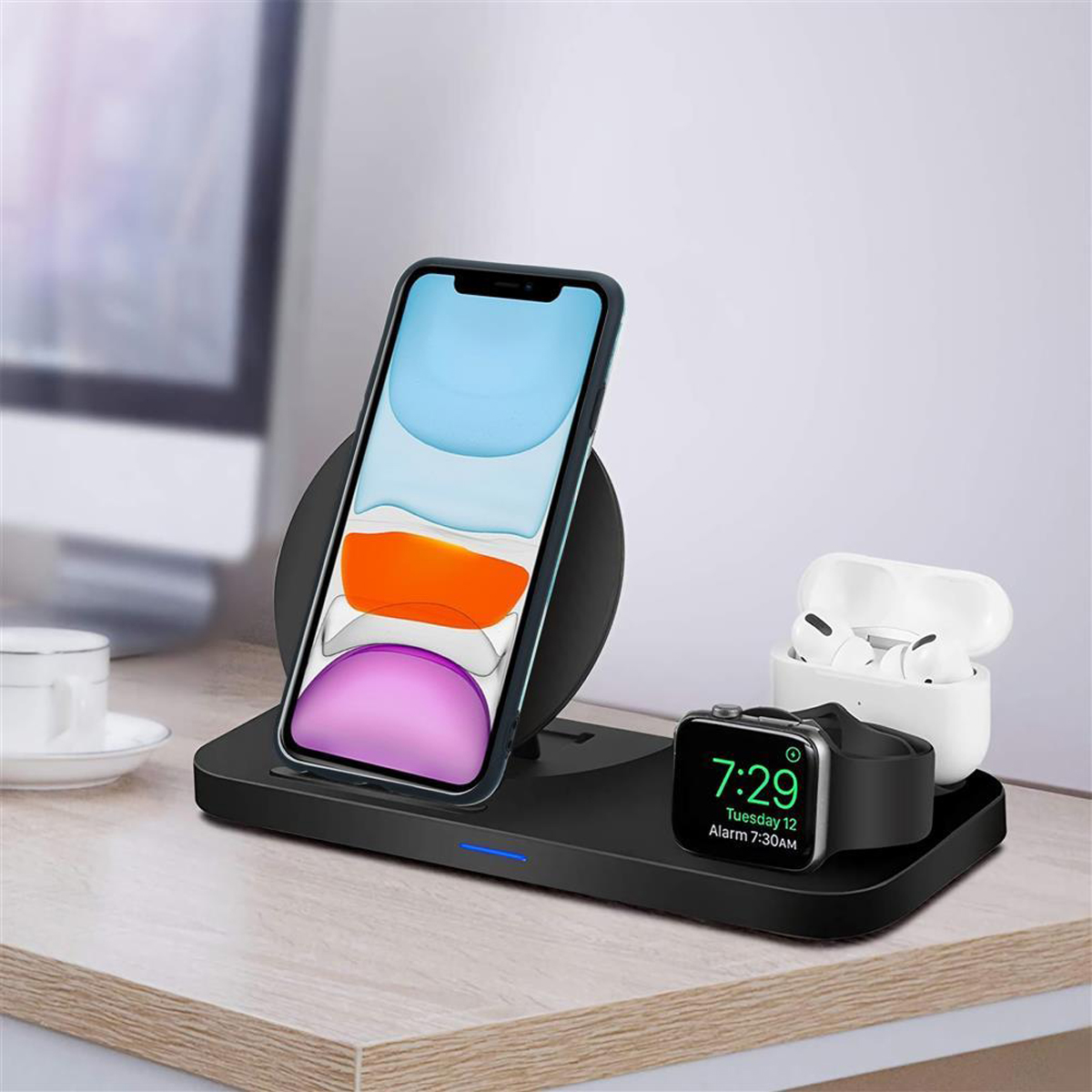 Una stazione di ricarica wireless con telefono, auricolari e smartwatch su una scrivania in legno.