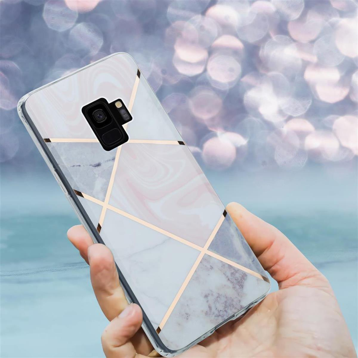 Una mano che tiene un telefono con una custodia a motivo marmorizzato bianco e linee geometriche dorate.