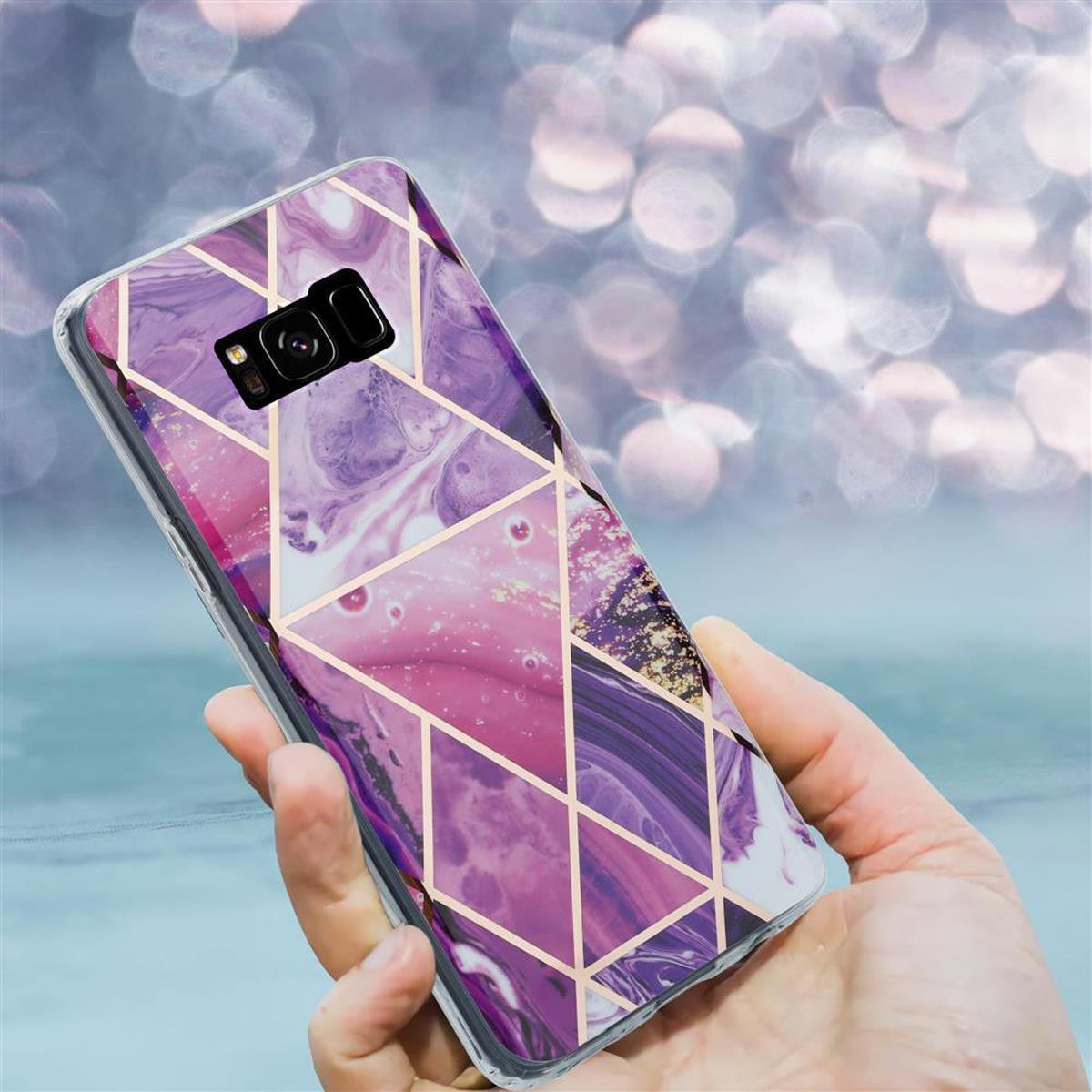 Custodia per telefono con design a marmo viola e rosa e linee geometriche dorate, tenuta in mano.