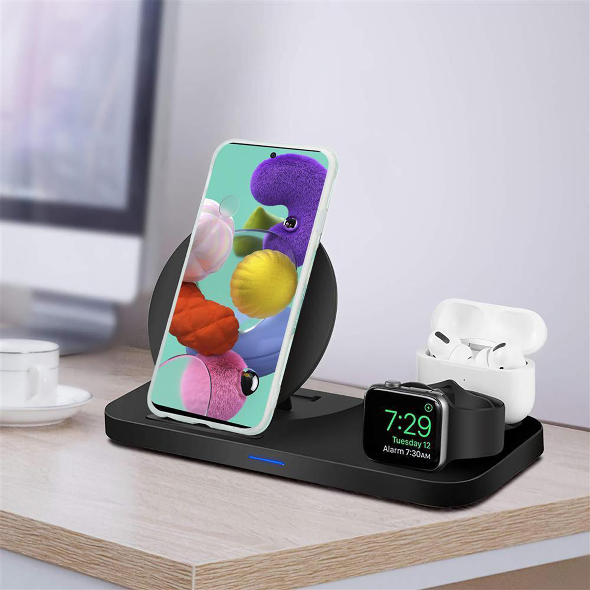 Una scrivania con telefono su caricabatterie wireless, orologio e auricolari. Il telefono mostra arte colorata.