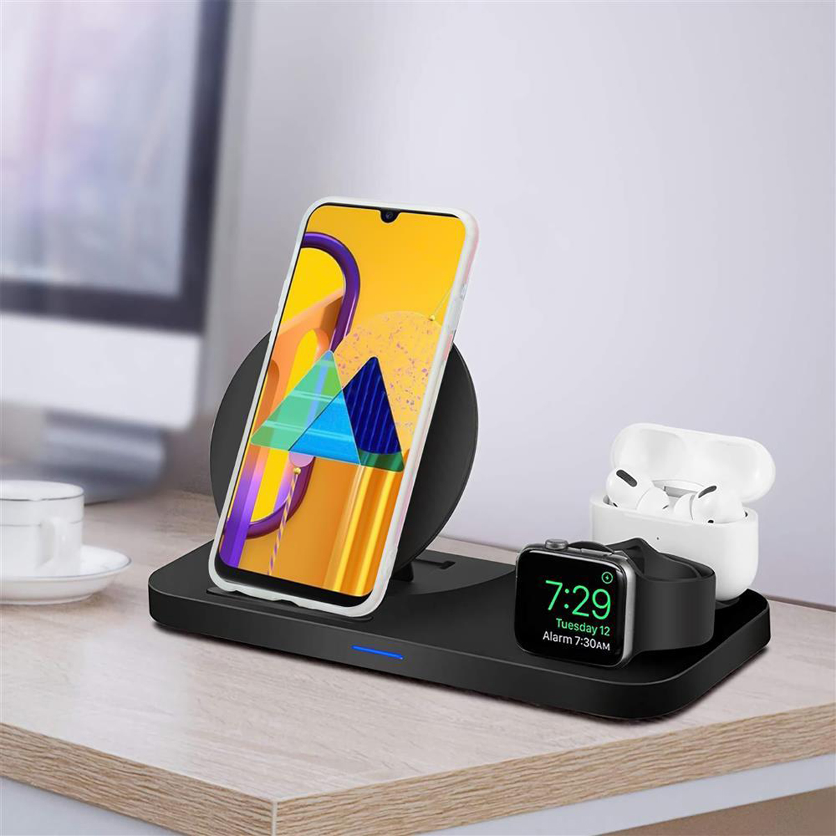 Una stazione di ricarica wireless con telefono, auricolari e smartwatch su una scrivania in legno.