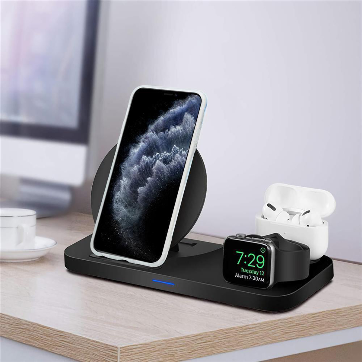 Stazione di ricarica wireless con telefono, orologio e auricolari. Articoli su una scrivania vicino a un computer e una tazza.