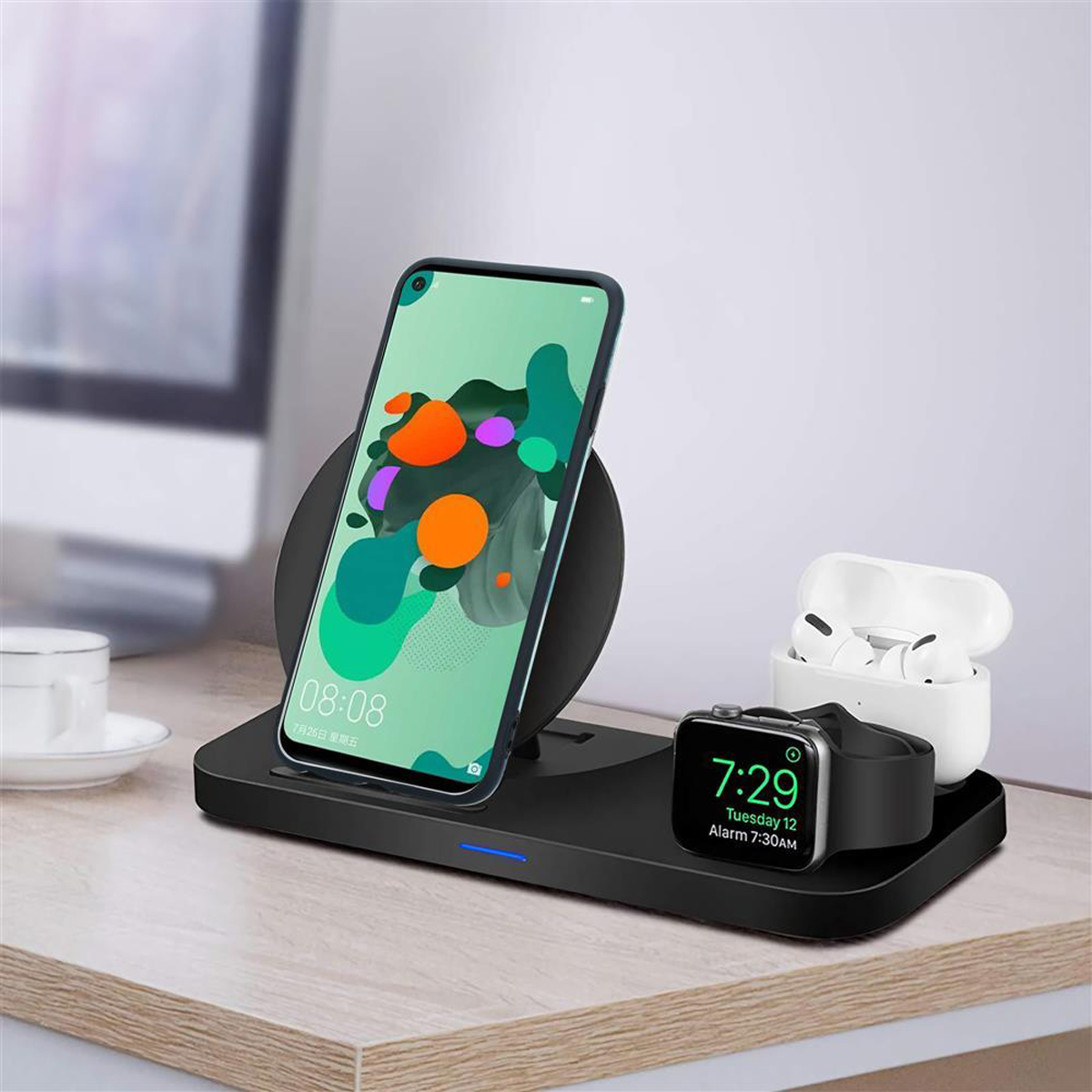 Caricabatterie wireless nero con telefono, orologio e auricolari. Il telefono mostra l'ora. Sfondo bianco.