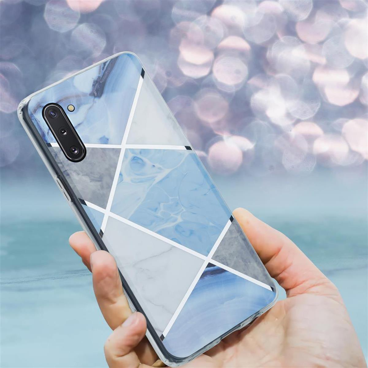 Mano che tiene una custodia per smartphone con un design a marmo blu e grigio. Linee geometriche bianche.