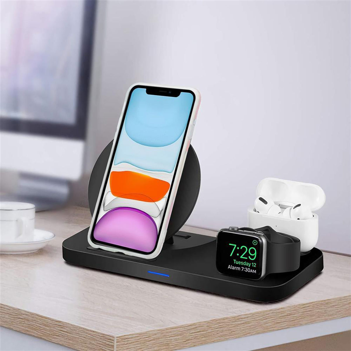 Stazione di ricarica wireless con telefono, auricolari e smartwatch su una superficie in legno.