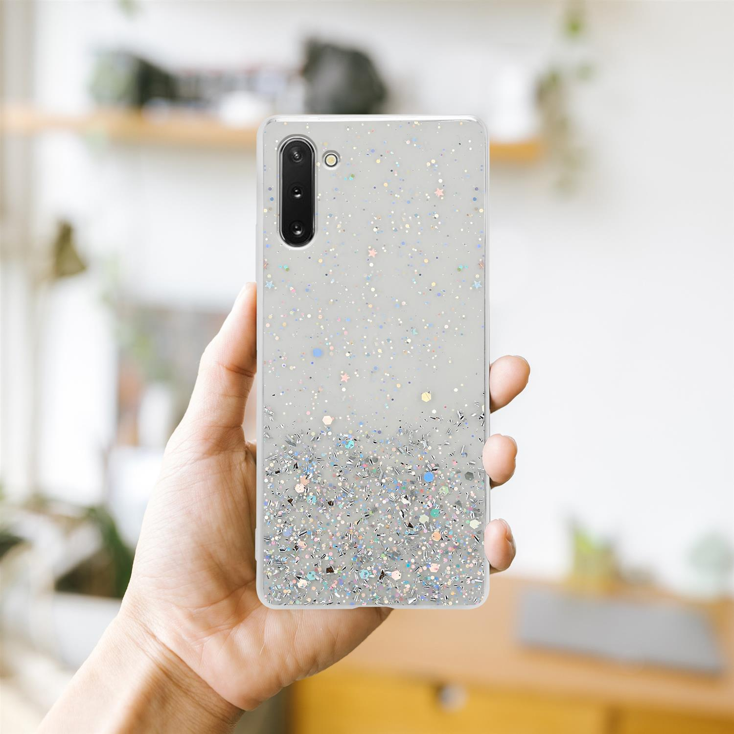 Mano che tiene una custodia per telefono con glitter, con uno sfondo sfocato di una stanza.