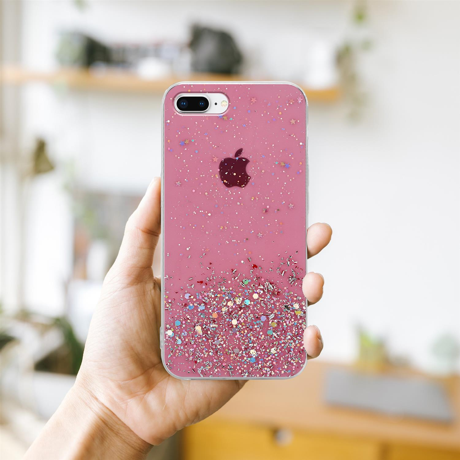 Eine Hand hält eine rosa glitzernde Handyhülle mit einem Apfel-Logo, vor einem verschwommenen Hintergrund.