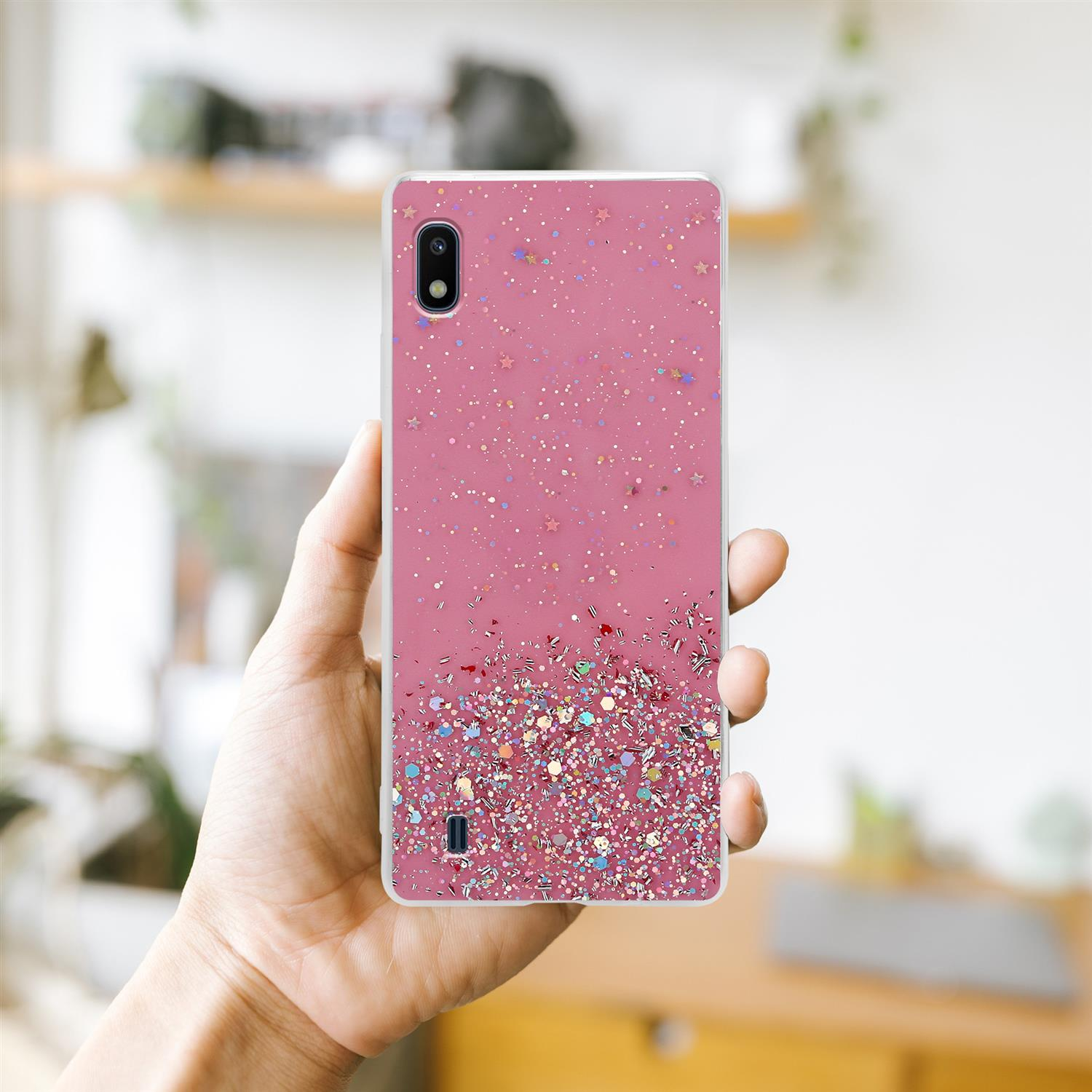 Handyhülle mit rosa Glitzer. Eine Hand hält das Telefon. Der Hintergrund ist ein Raum.