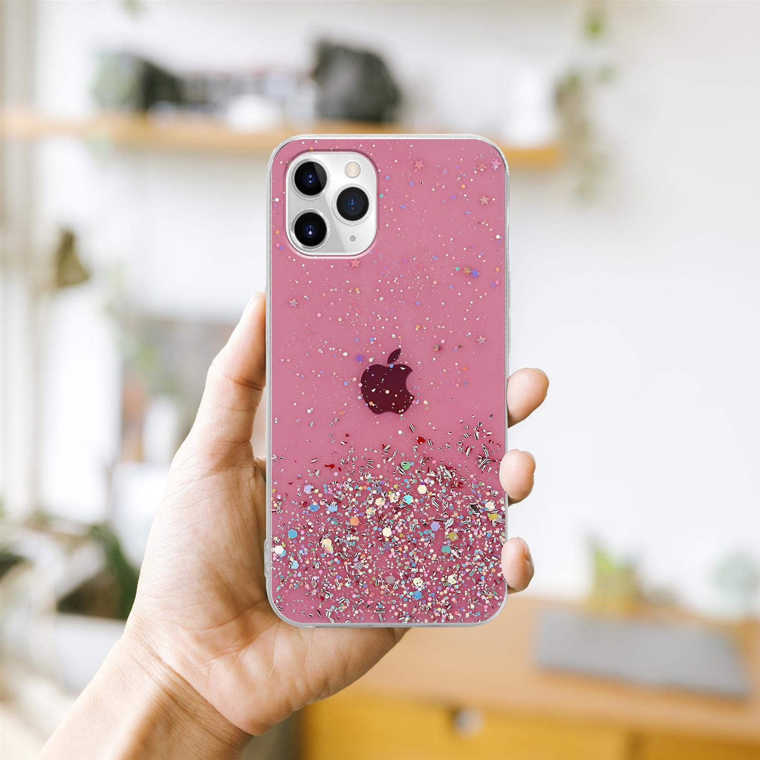 Telefon mit rosa Glitzerhülle in einer Hand gehalten. Der Hintergrund ist eine verschwommene Innenszene.