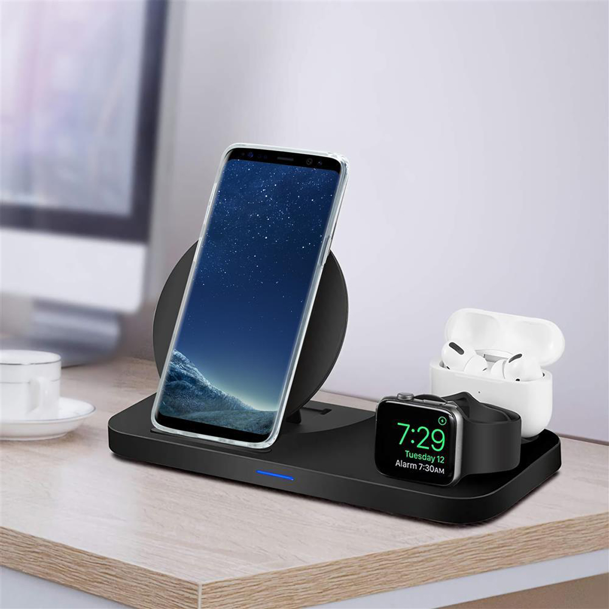 Stazione di ricarica wireless con telefono, AirPods e Apple Watch. Scrivania in legno, sfondo bianco.