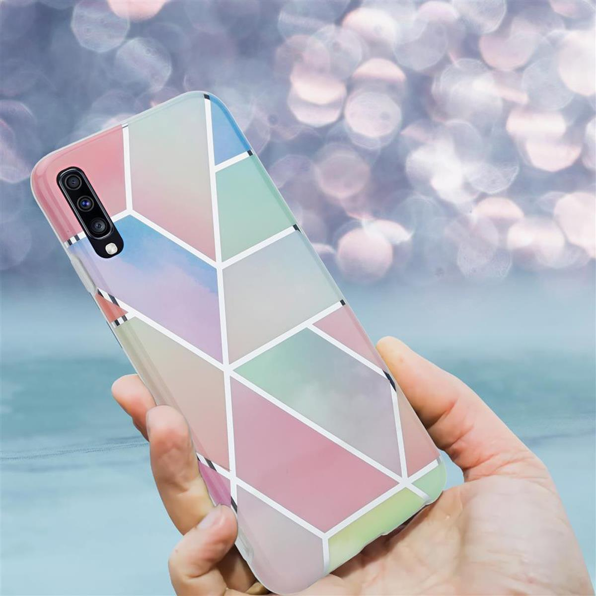 Mano che tiene custodia per telefono con design geometrico, colori pastello e linee bianche. Sfondo bokeh.