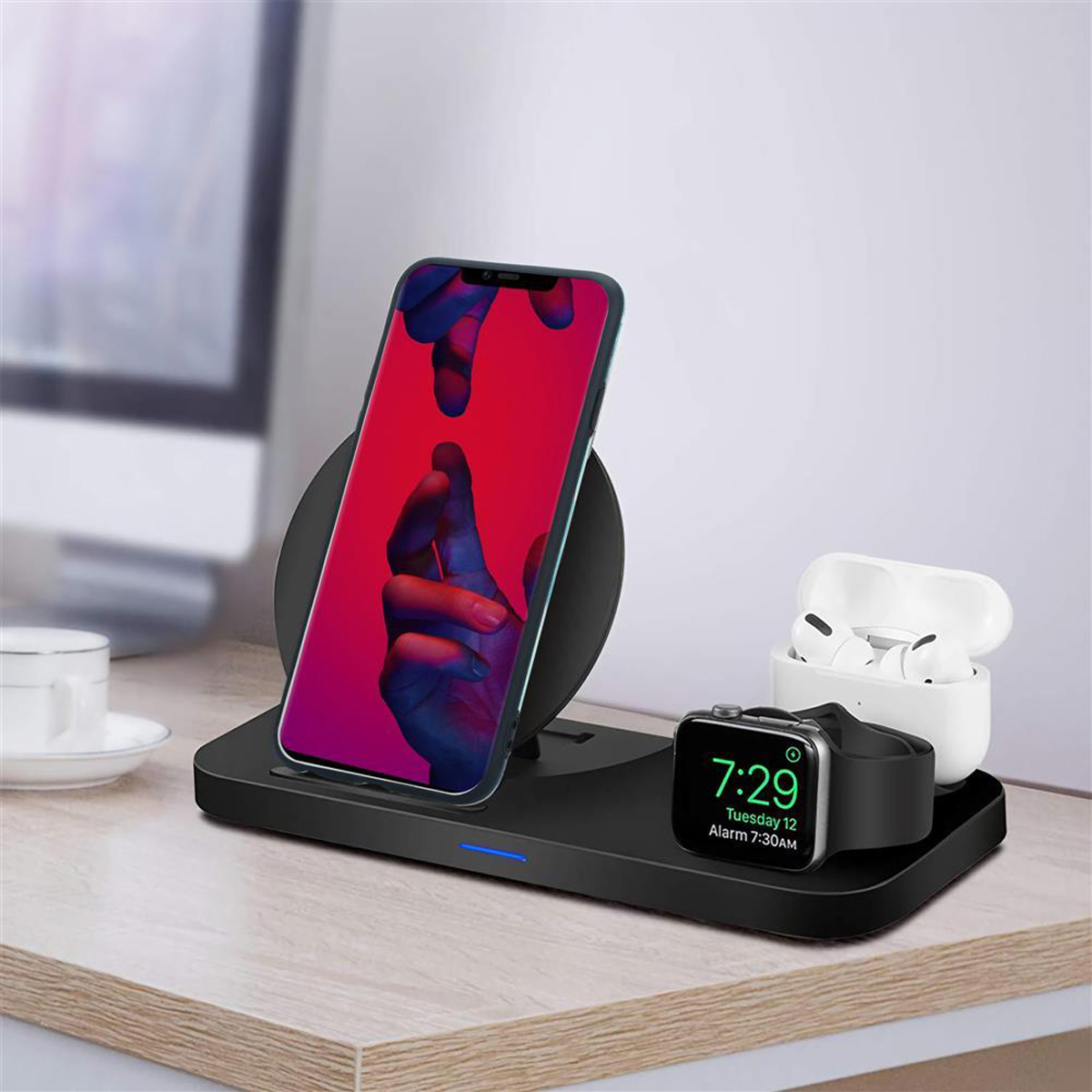 Stazione di ricarica wireless con telefono, orologio e auricolari, su un tavolo di legno.