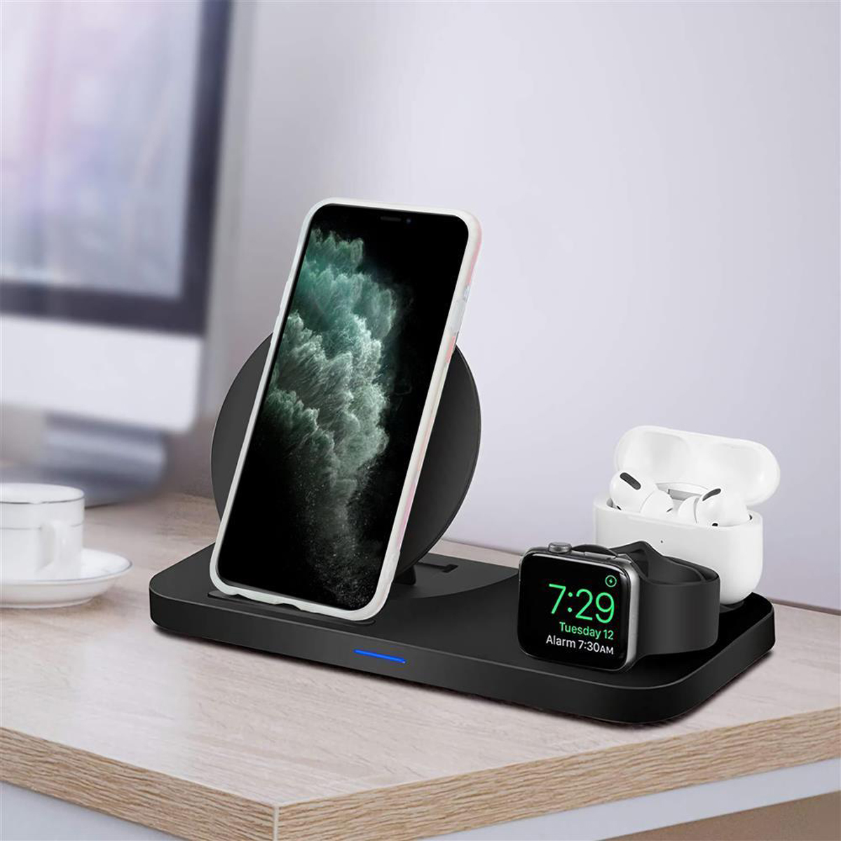 Stazione di ricarica wireless con telefono, auricolari e smartwatch su una scrivania. Sfondo: monitor.