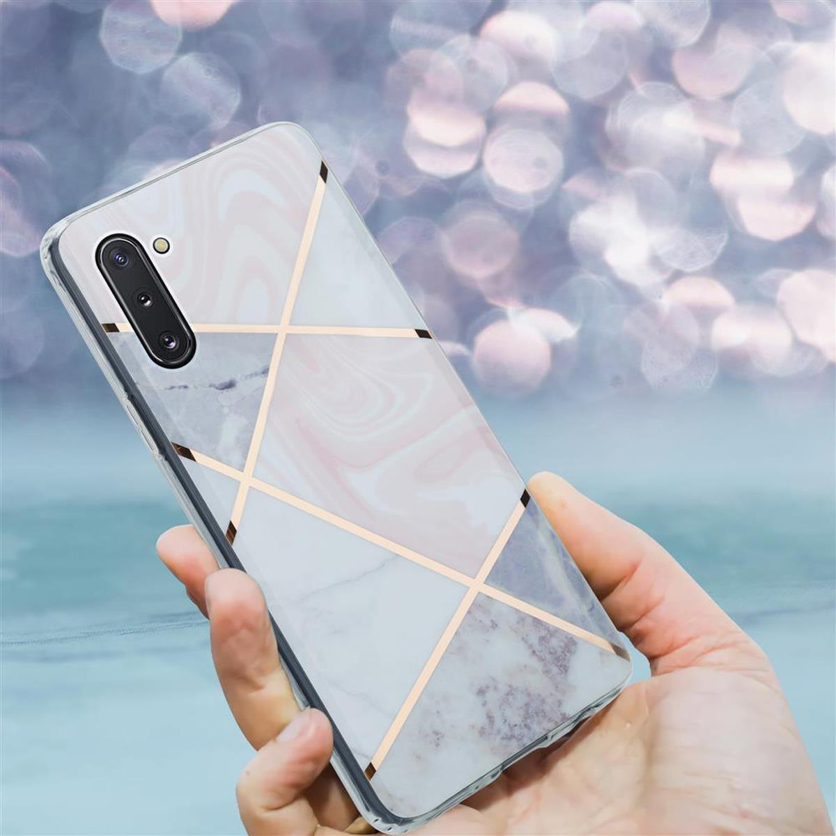 Mano che tiene una custodia per telefono con un design a marmo e linee geometriche dorate.