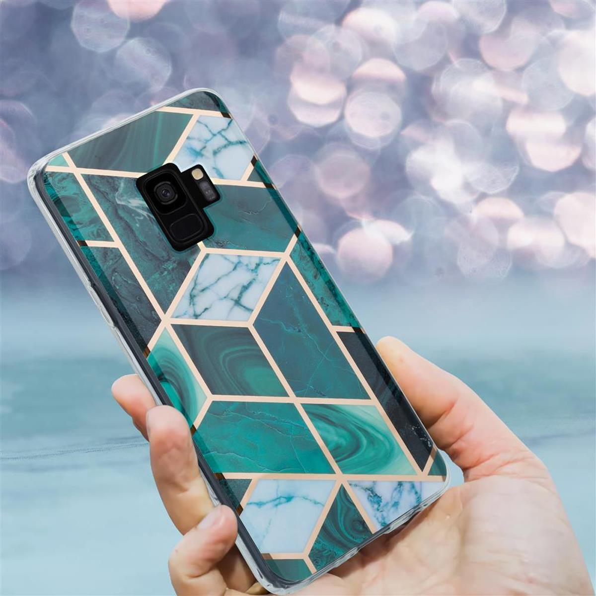Custodia per telefono verde e oro con motivo geometrico tenuta in mano su sfondo sfocato.