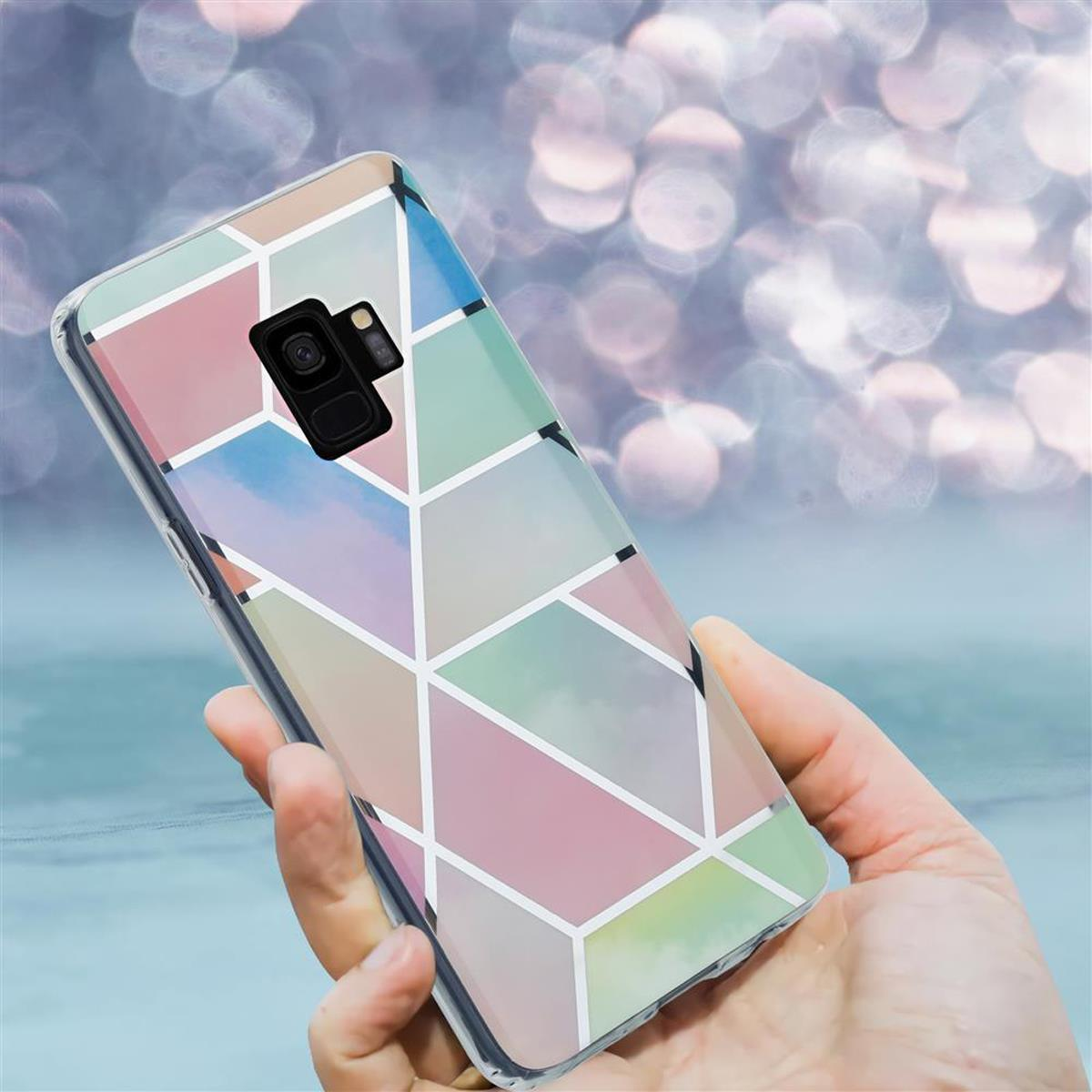 Mano che tiene uno smartphone con una custodia dal design geometrico colorato. Sfondo sfocato.