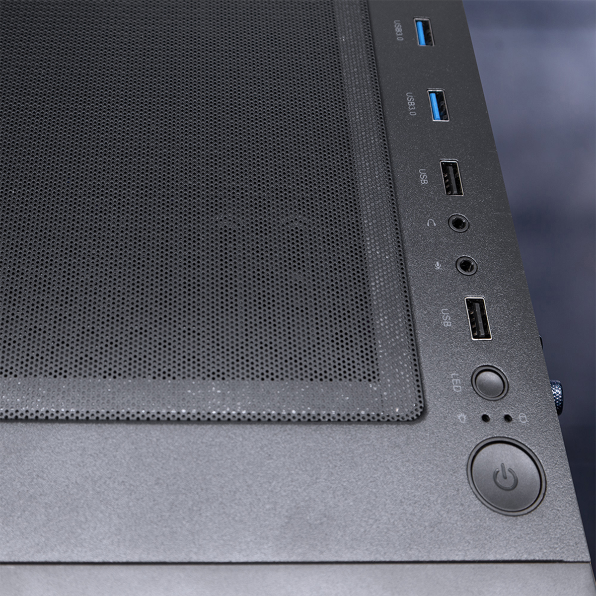 Nahaufnahme eines Computergehäuses mit Mesh-Front, mehreren Anschlüssen und einem Power-Button.