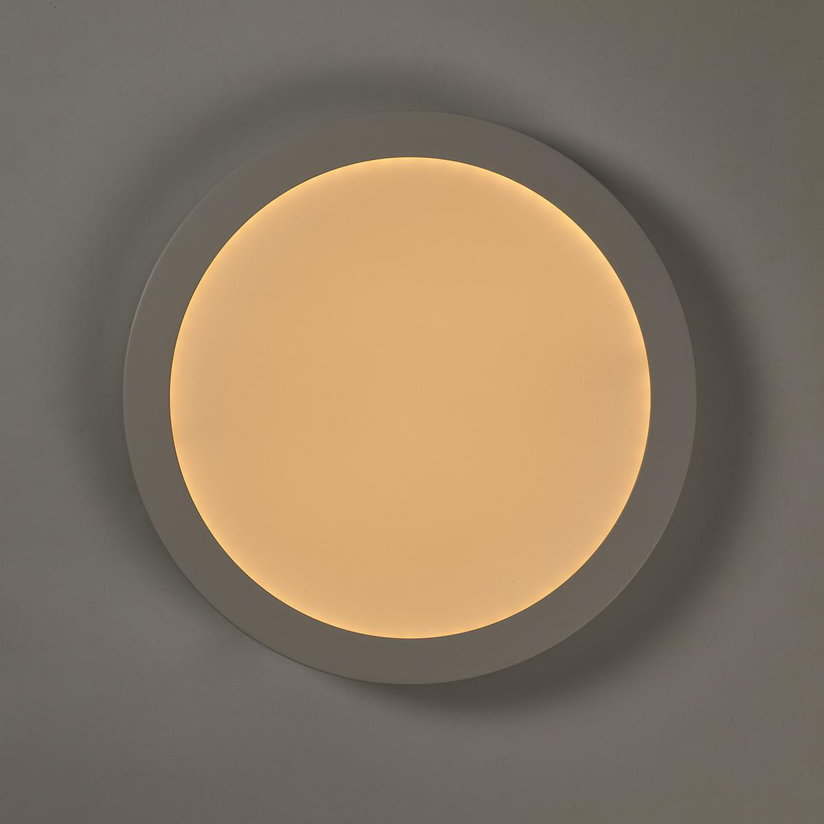 Una luce da soffitto a LED circolare bianca contro un muro grigio, che illumina lo spazio.