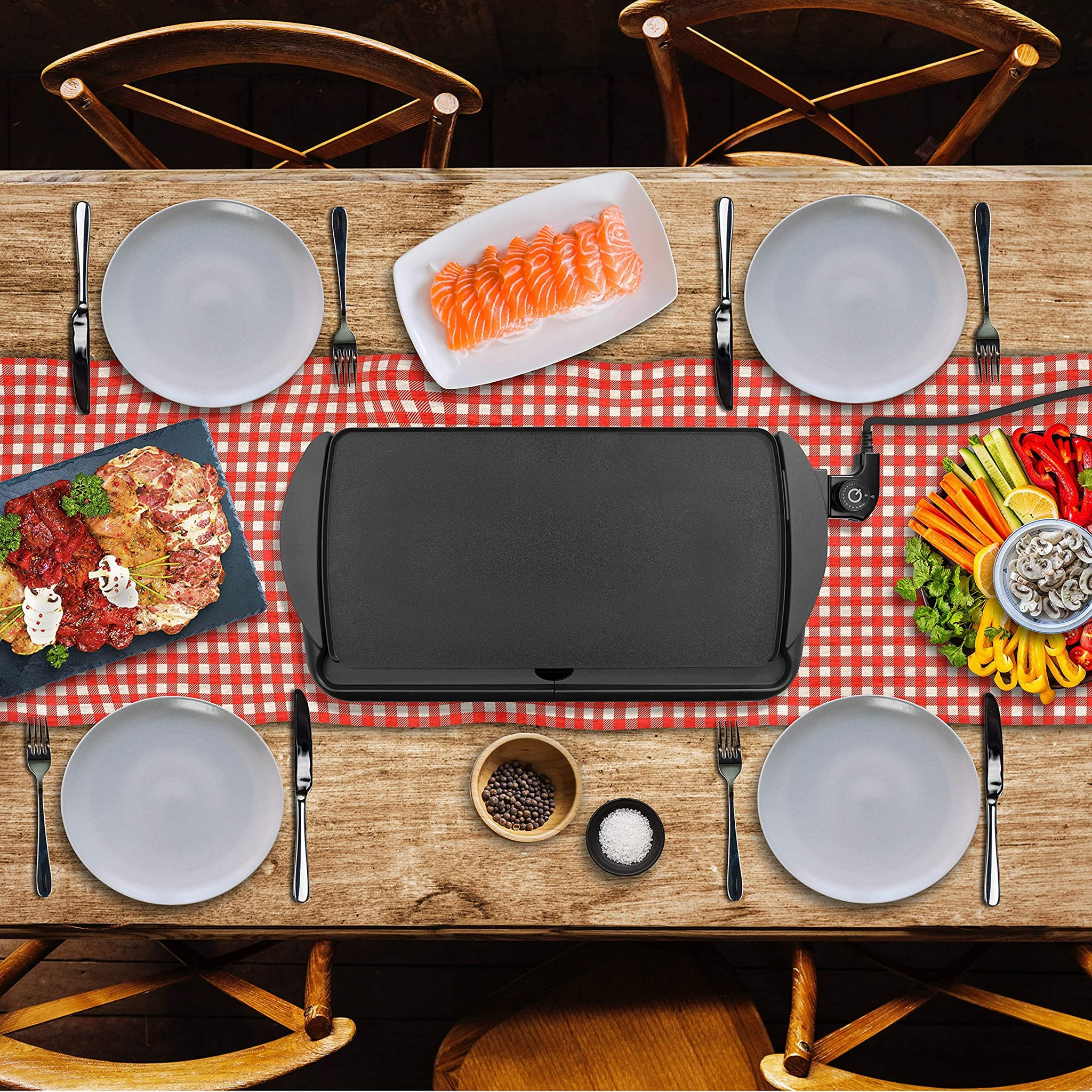 Ein Tisch, der für eine Mahlzeit gedeckt ist. Er hat einen Grill, Teller, Essen und Besteck.