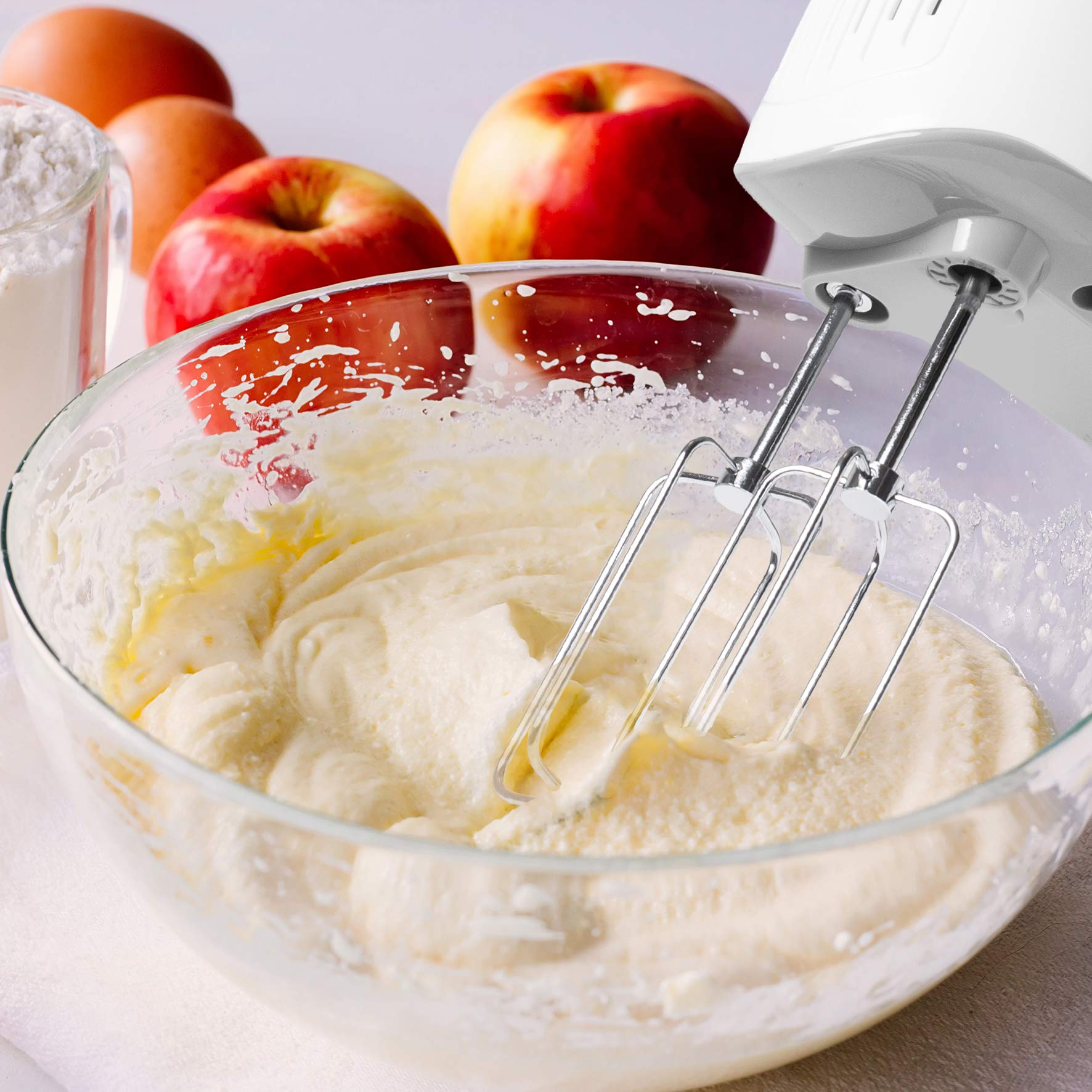 Rührschüssel mit Teig. Eier, Äpfel und Mehl im Hintergrund. Elektrischer Mixer.