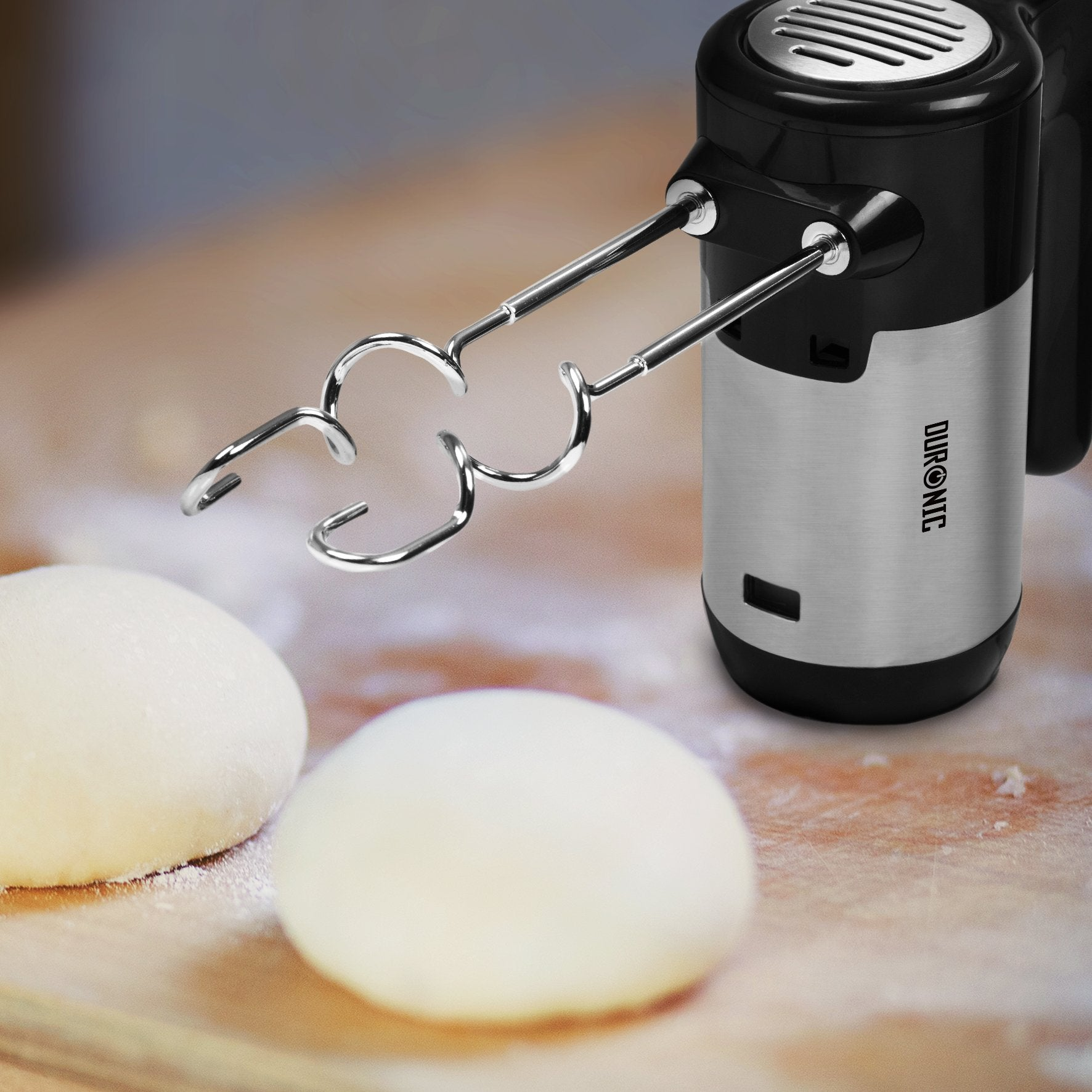 Elektrischer Mixer mit zwei Teigkugeln auf einer Holzoberfläche. Der Mixer ist schwarz und silber.