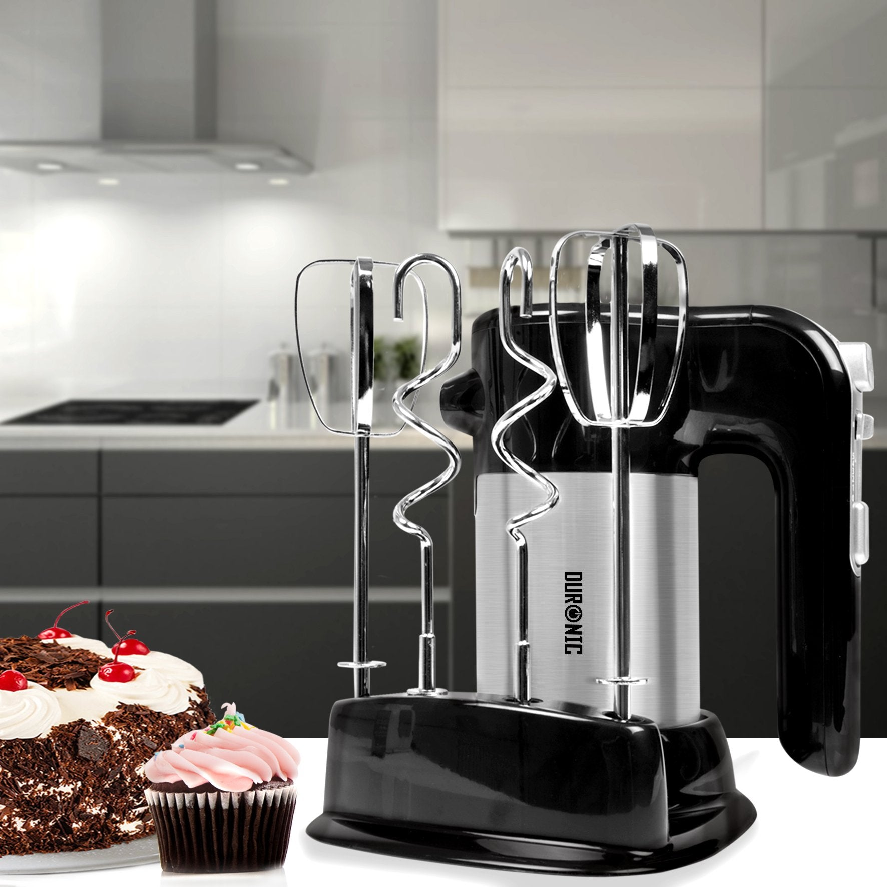 Ein schwarzer und silberner Handmixer auf einem weißen Tisch neben einem Kuchen und einem Cupcake.